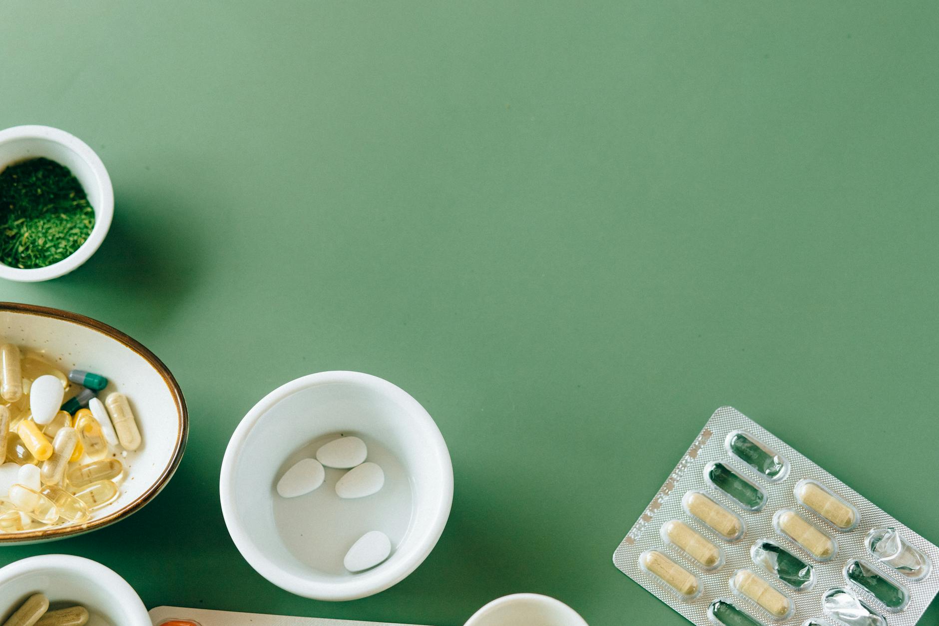 A flat lay of assorted pills and herbs on a green background emphasizing natural health remedies. - spring slump remedies