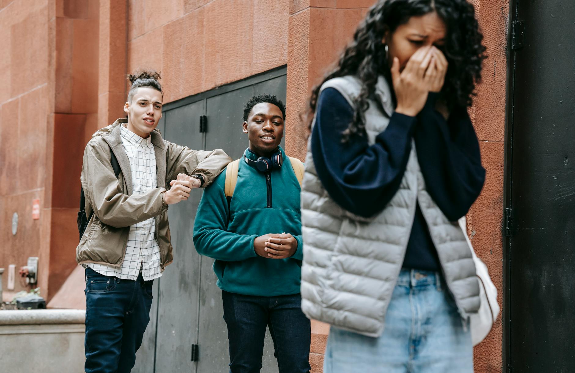 Low angle of annoyed young ethnic lady covering mouth and crying after being abused by rebellious multiracial male groupmates - spring social anxiety
