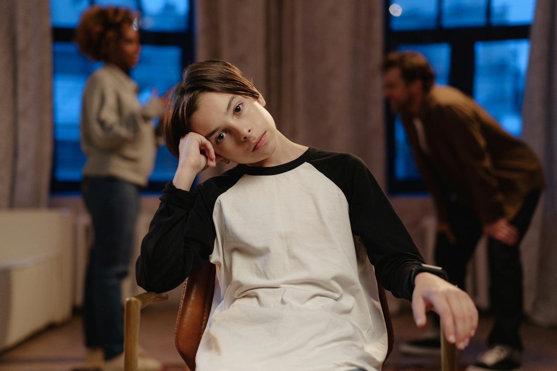 A young boy in a black and white shirt looks sad as his parents argue in the background. - spring stress families