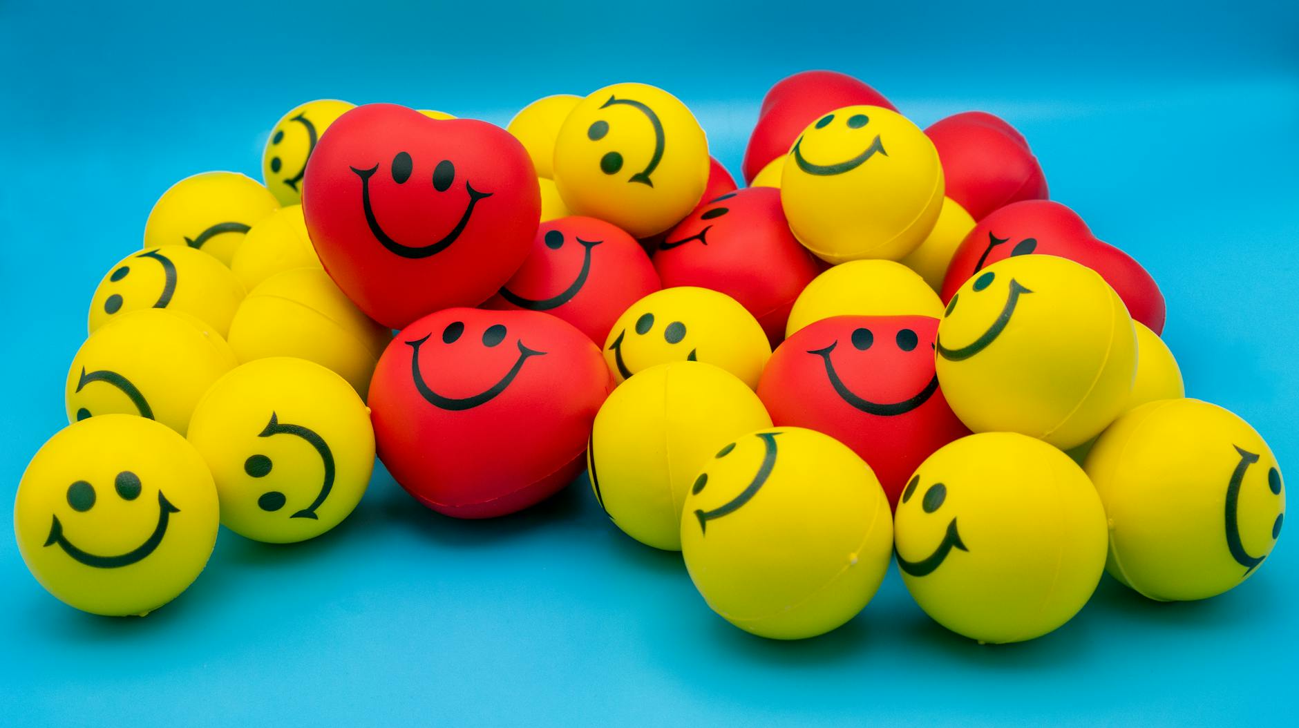 A collection of vibrant yellow and red smiley stress balls arranged on a blue surface. - spring stress relief