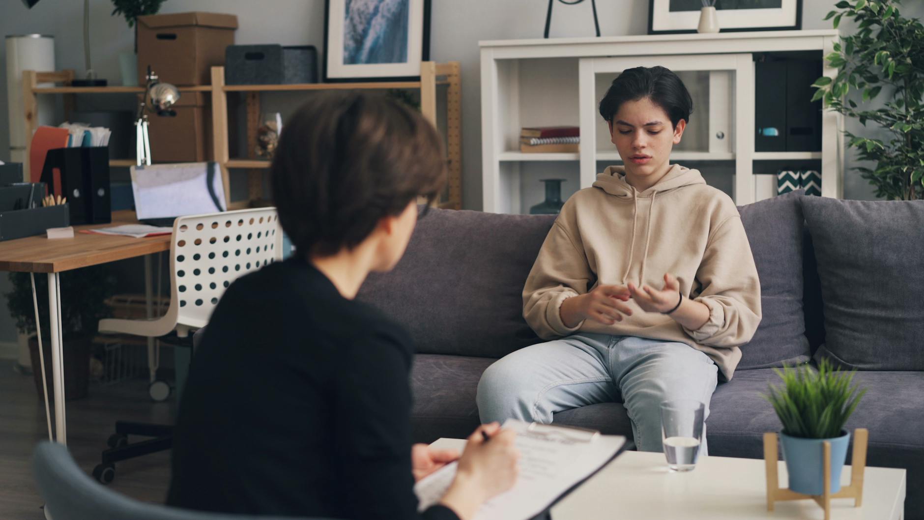 A teenager engages in a therapy session with a professional counselor in a modern office setting. - teen mental health