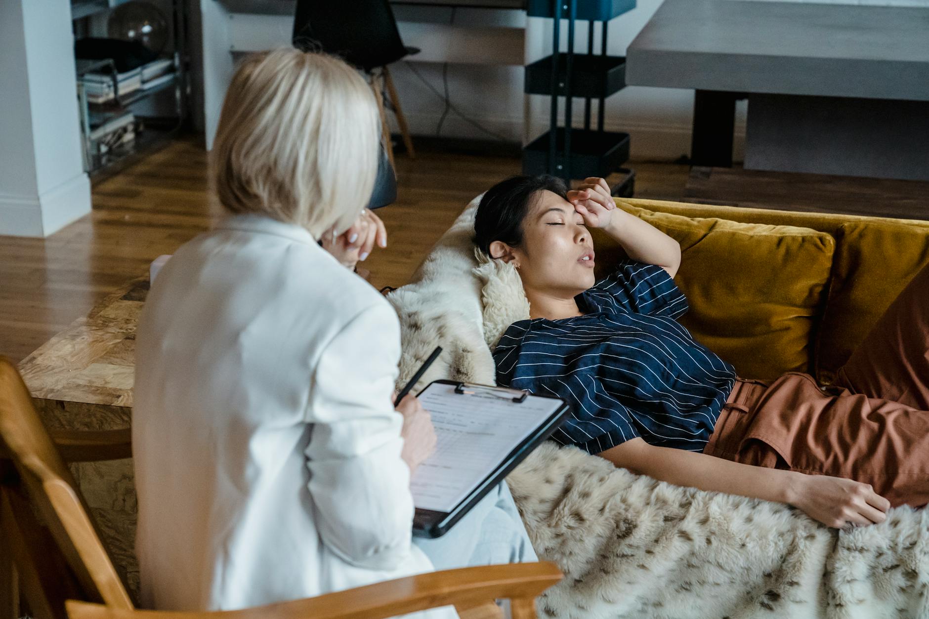 Woman in therapy session lying on couch, discussing emotions with a therapist taking notes. - therapist for seasonal anxiety