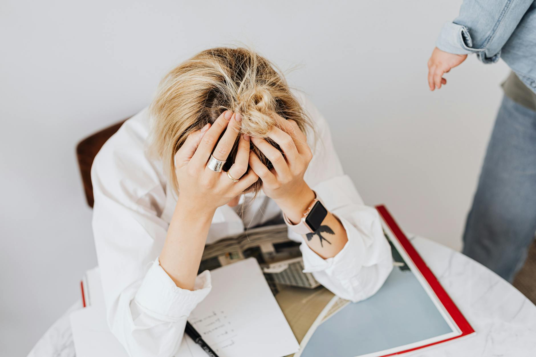 Frustrated woman in white shirt sitting with head in hands, overwhelmed by work tasks. - therapy for burnout