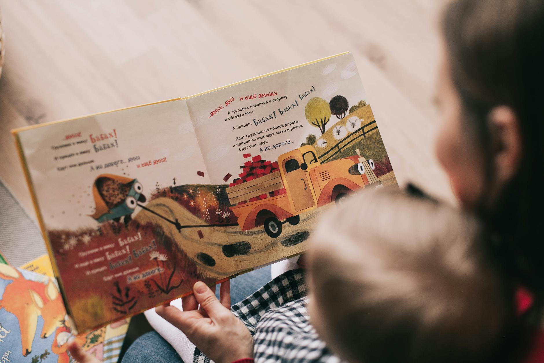 A mother and toddler sharing a story from an illustrated children's book indoors. - toddler language development