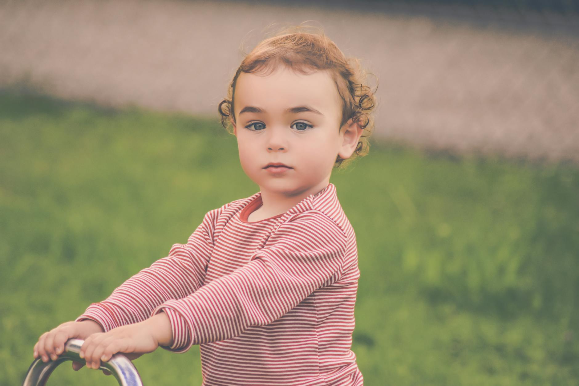 Adorable young child with curly hair playing outdoors in a striped shirt, enjoying a sunny day. - toddler outdoor independence