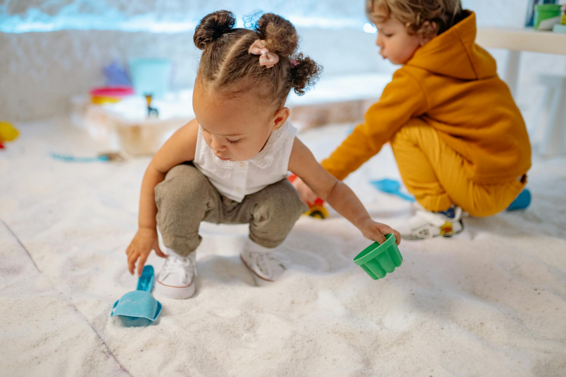 Two kids enjoying a fun indoor sand play session with colorful toys. - toddler playdate skills