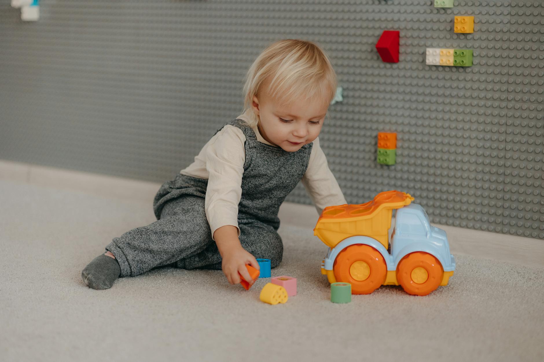 Cute toddler engaged with colorful blocks and toy truck indoors. - toddler playdate skills