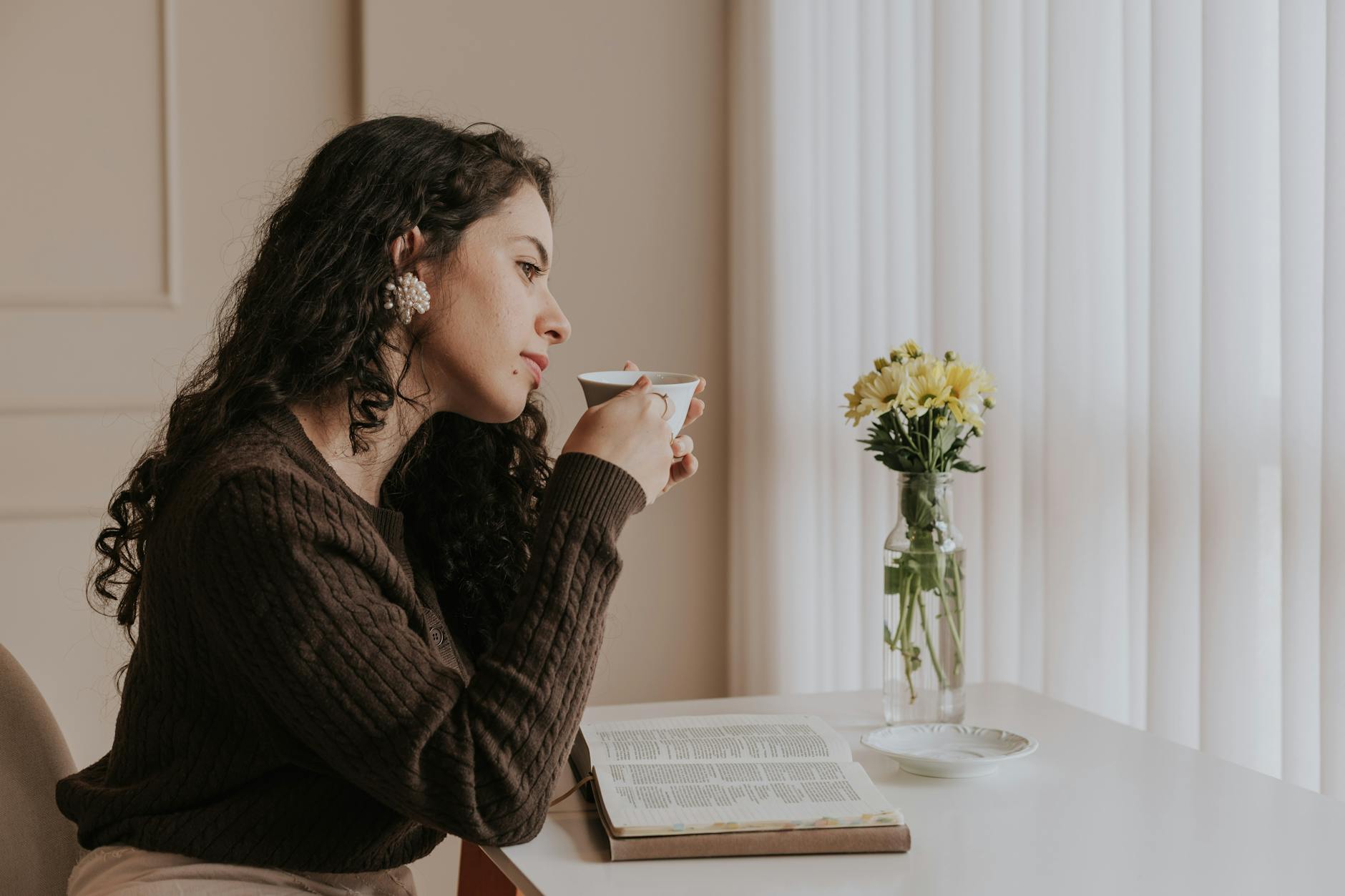 A woman relaxes with tea and a book by a bright window, embracing a peaceful moment. - virtual therapy benefits