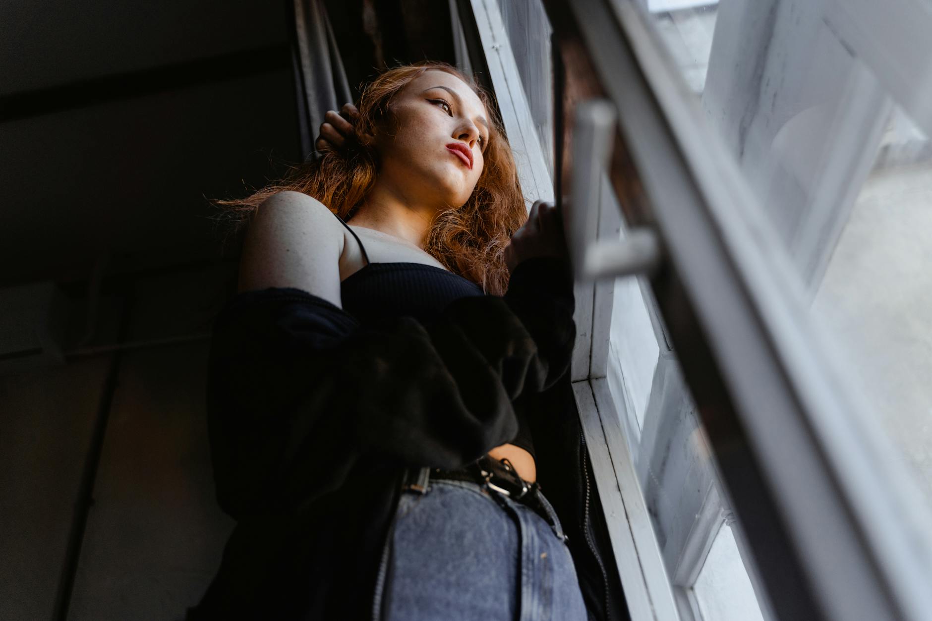A woman gazes out of a window, deep in thought in a softly lit room. - winter depression mindfulness