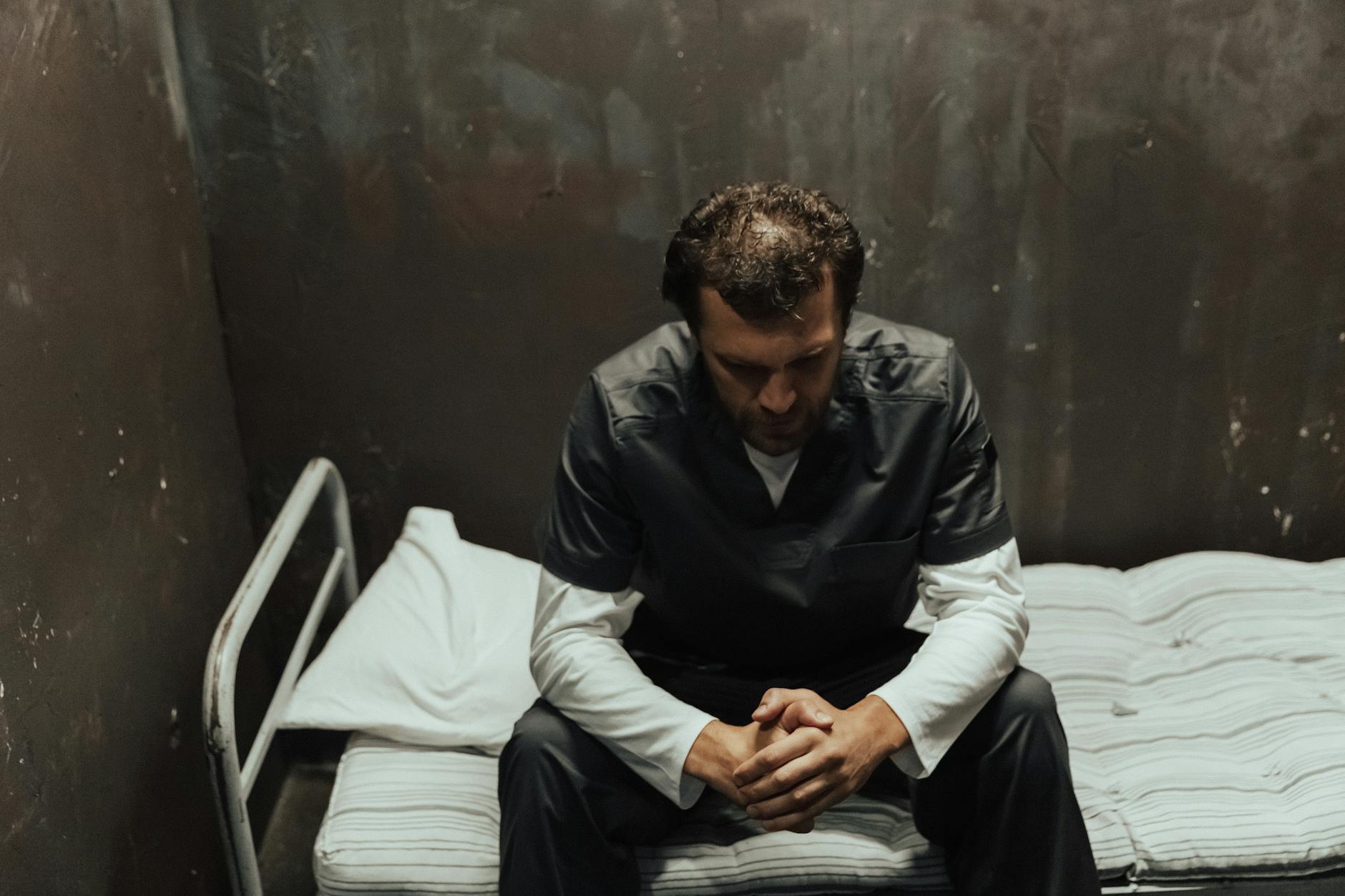 A male prisoner sits thoughtfully on the bed in a dimly lit cell, reflecting on life. - winter depression mindfulness