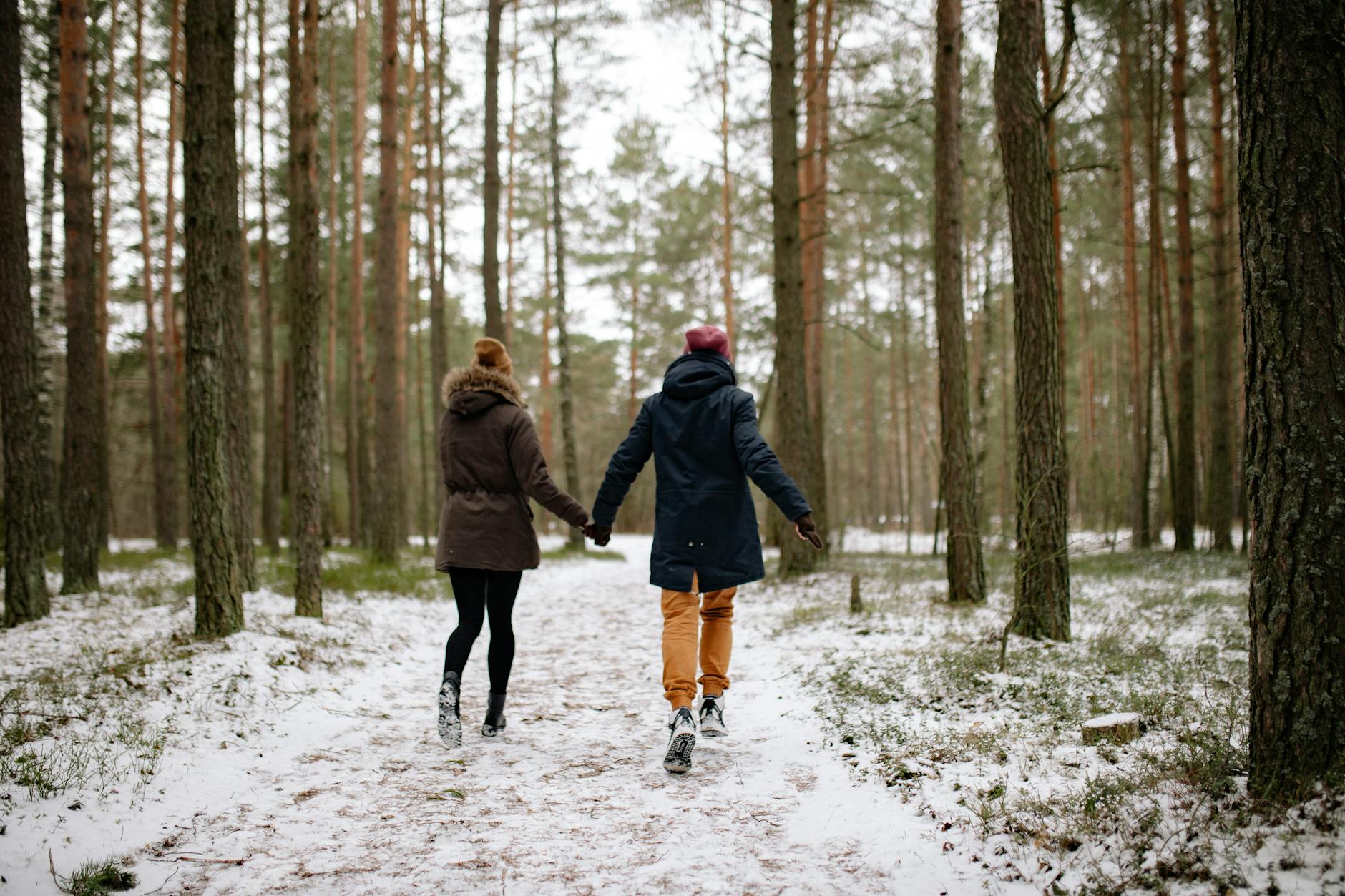 A couple walking hand in hand through a snowy forest path in winter. - winter relationship activities