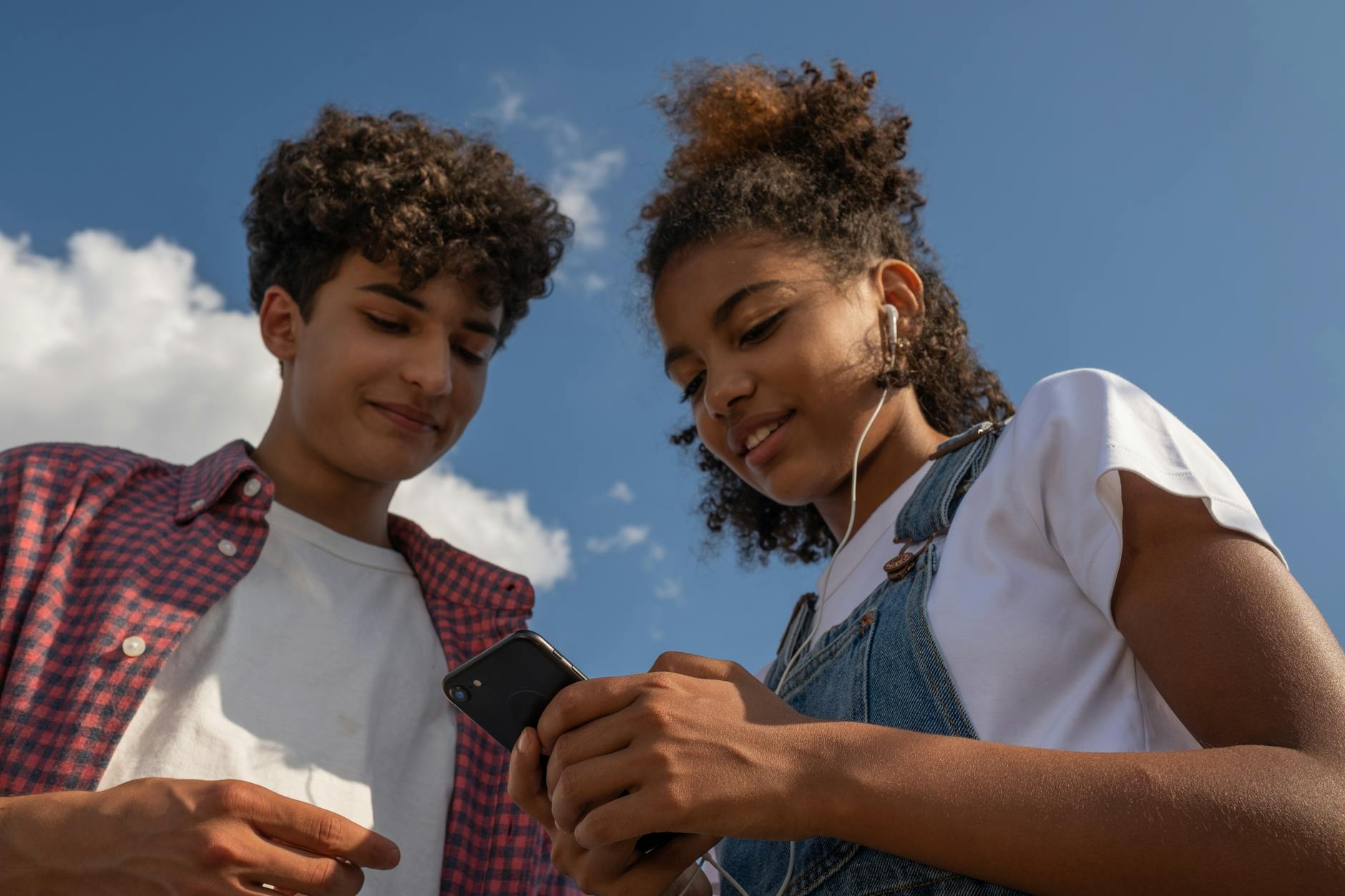 Two teenagers enjoy music together outdoors using a smartphone and earphones. - active listening teens