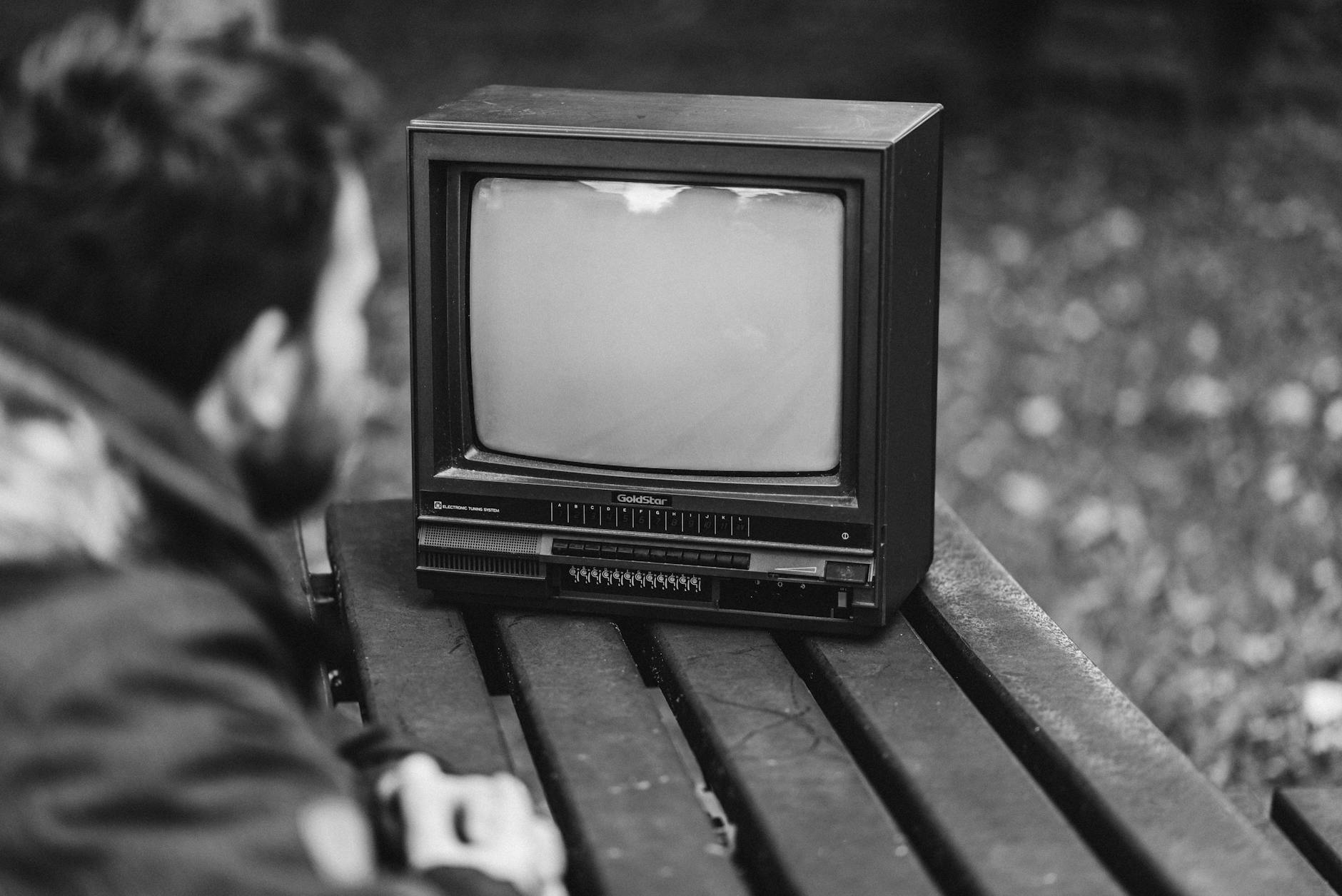 Black and white side view of anonymous male sitting at wooden table and looking at old fashioned television in nature on blurred background - anger management tv shows