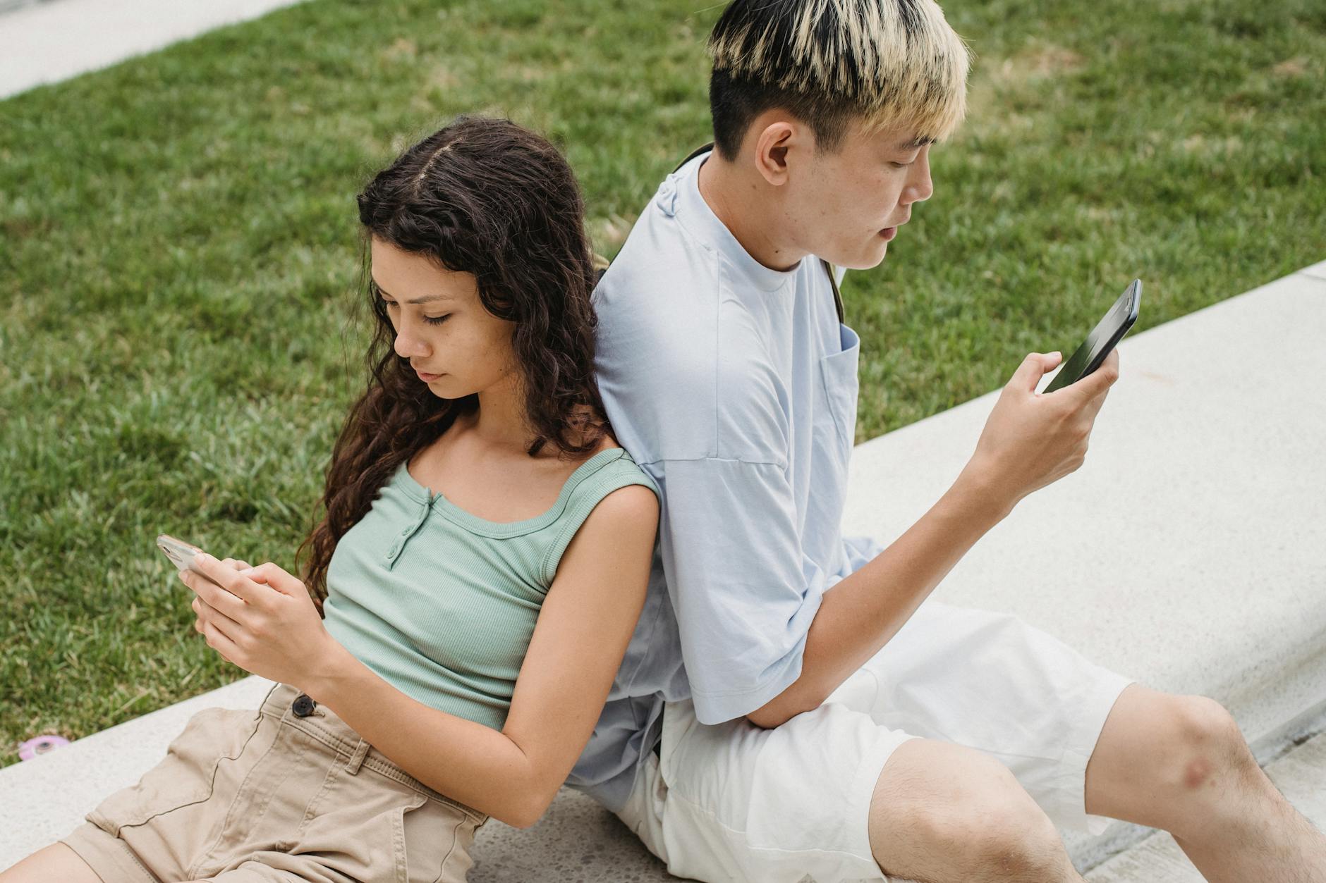 From above of crop diverse couple text messaging on cellphones while sitting on bench near lawn in daylight - couple communication needs
