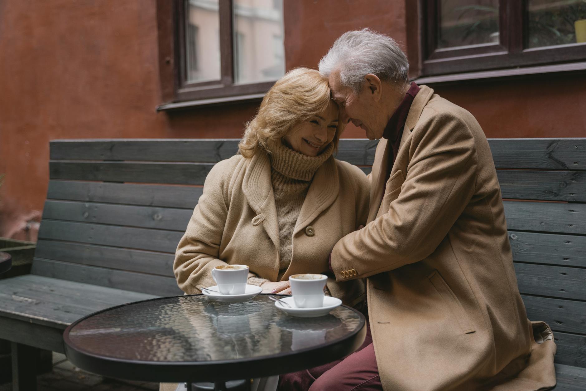 Lovely elderly couple sharing coffee on a cozy outdoor bench, expressing warmth and affection. - dating in 40s