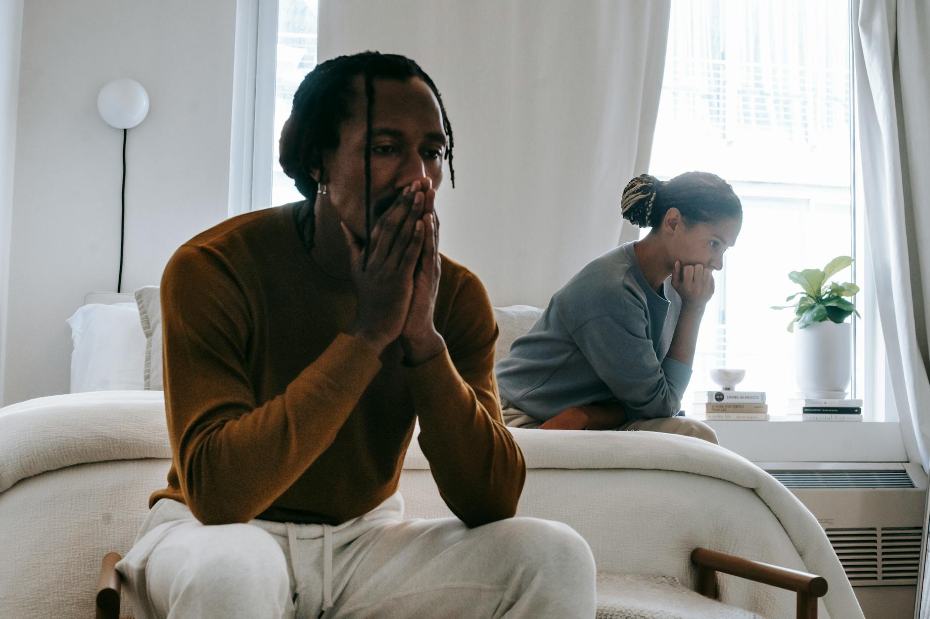 Wistful concerned African American couple in casual clothing sitting on bed at home after having quarrel - declutter relationship conflict