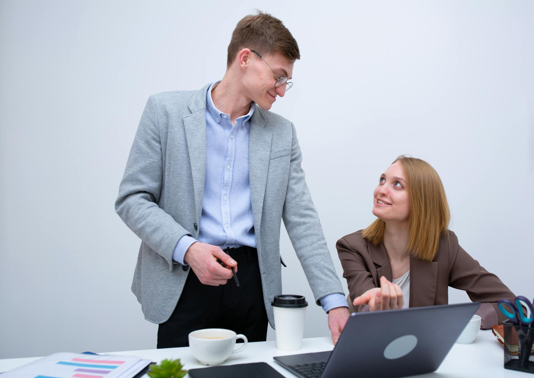 Two colleagues collaborating at a white desk with laptops and documents in an office setting. - effective communication skills