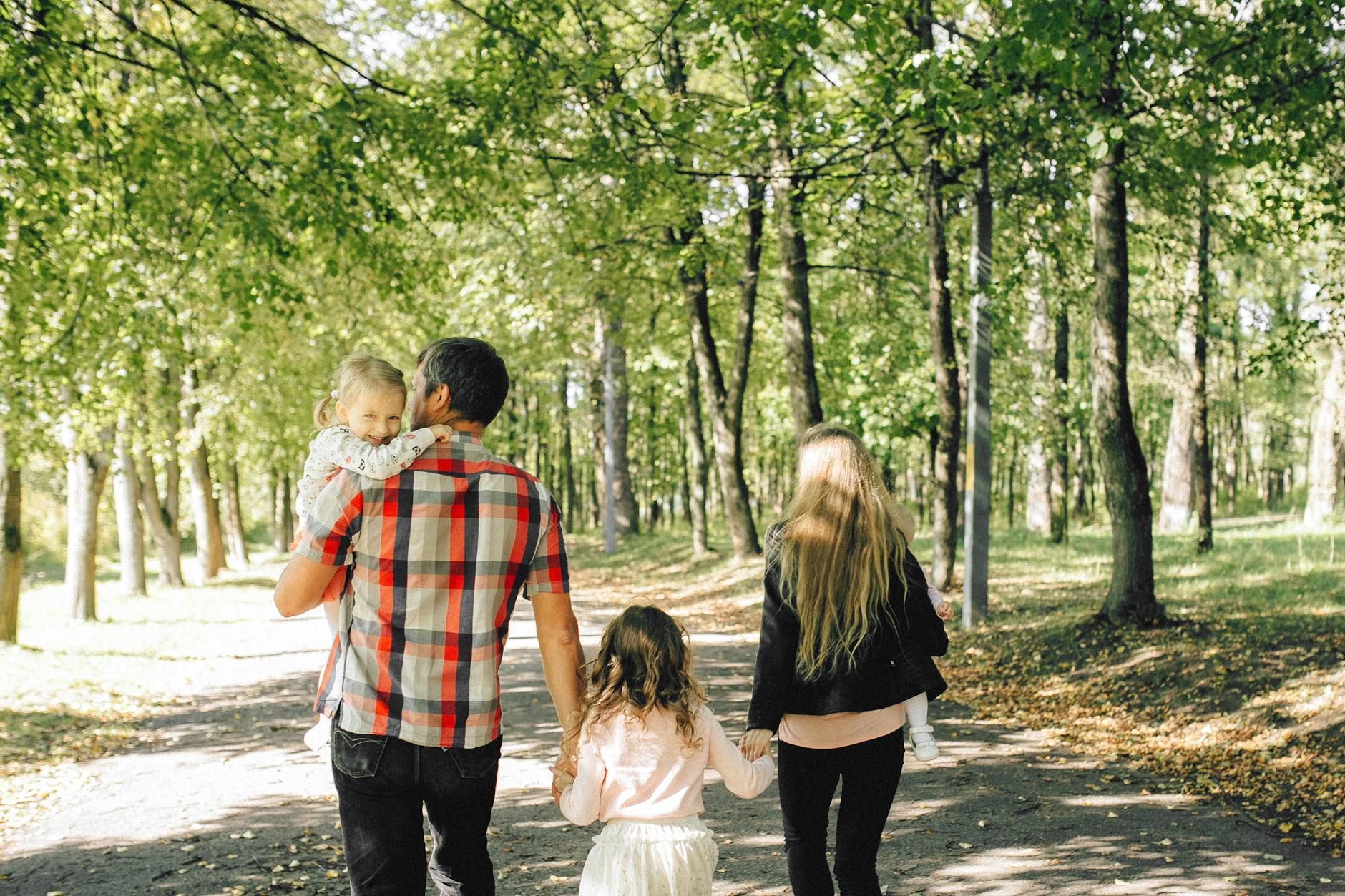 A family of four walking through a sunlit park, embracing togetherness and nature. - family therapy spring
