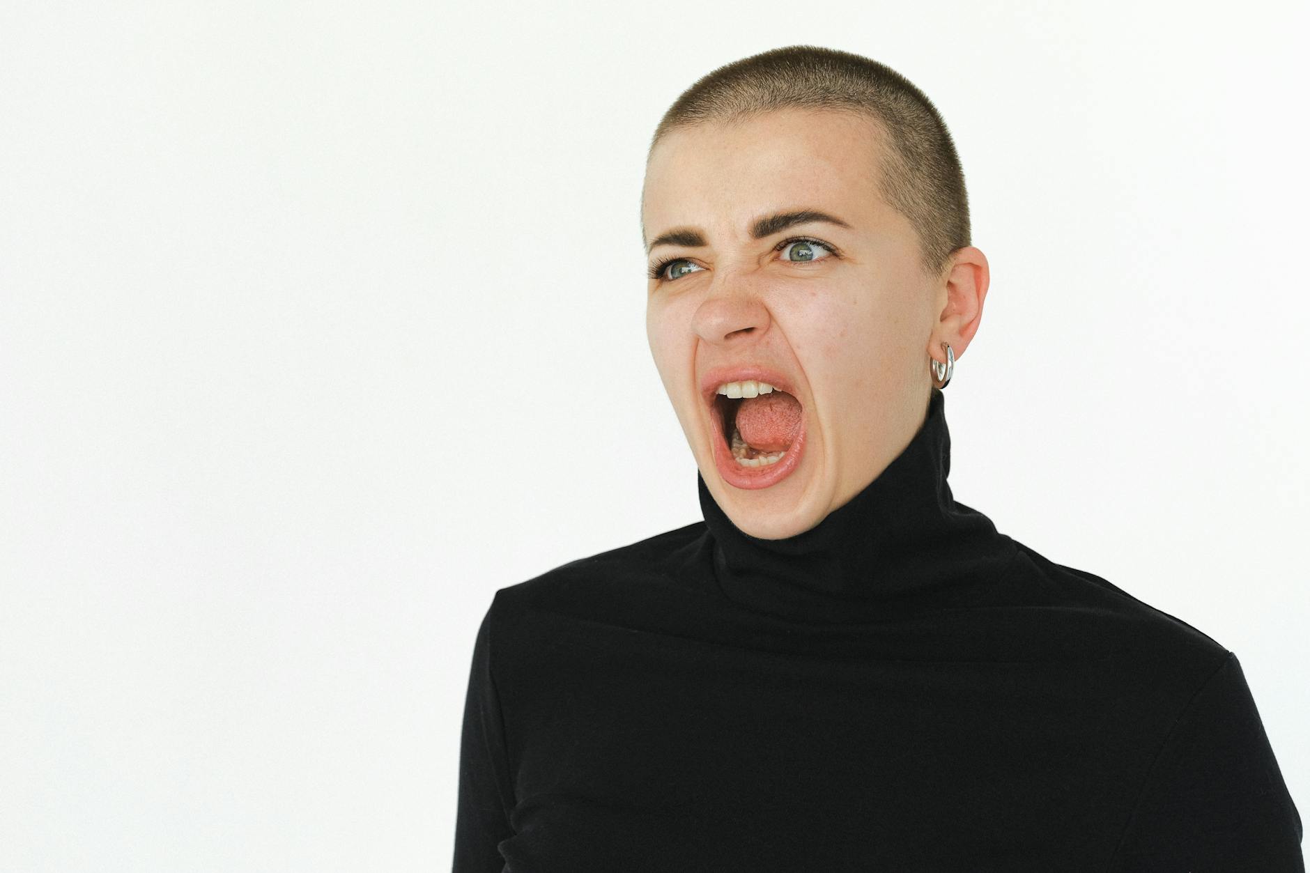 A woman yells expressively in a studio setting, wearing a black turtleneck. - free anger management