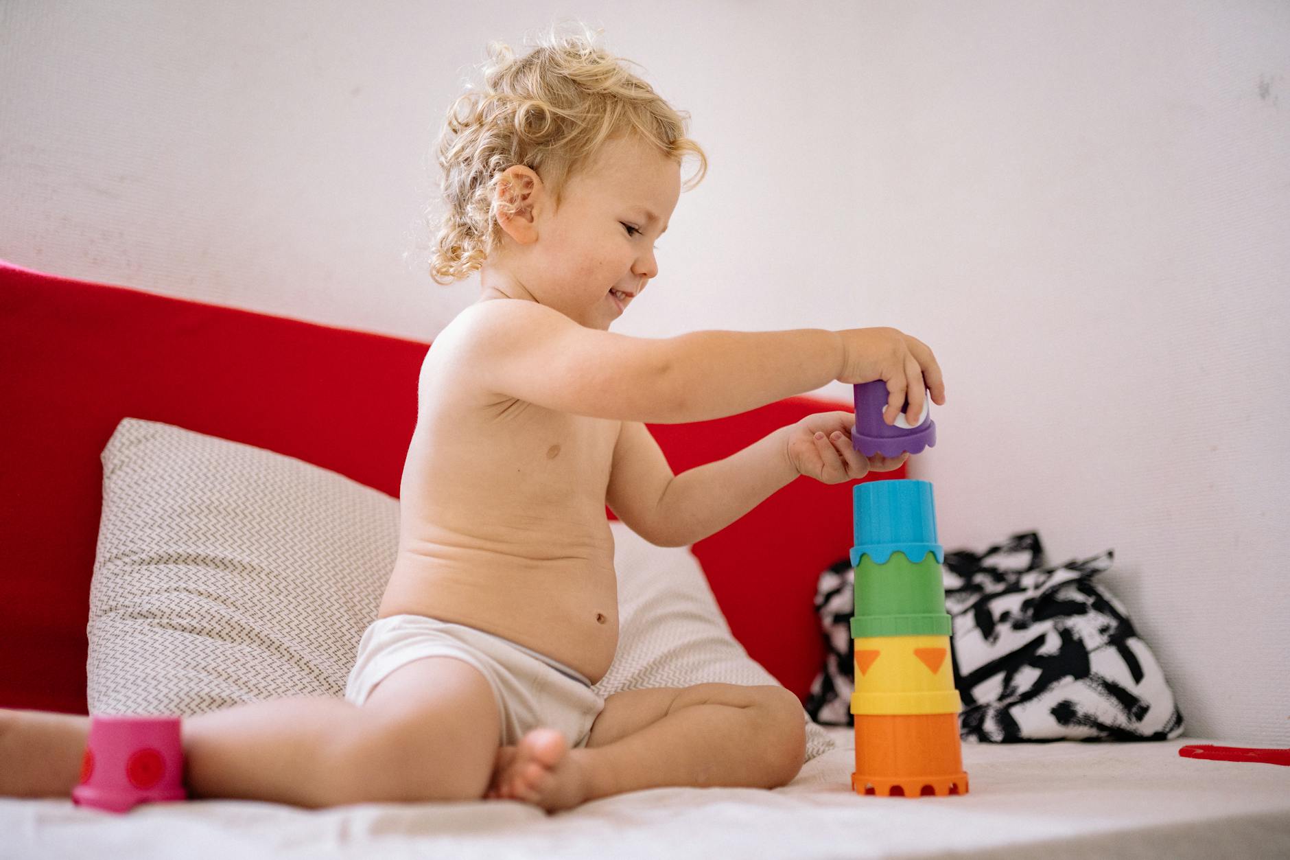A cheerful toddler building a tower with colorful plastic stacking toys on a sofa. - independent play toddler