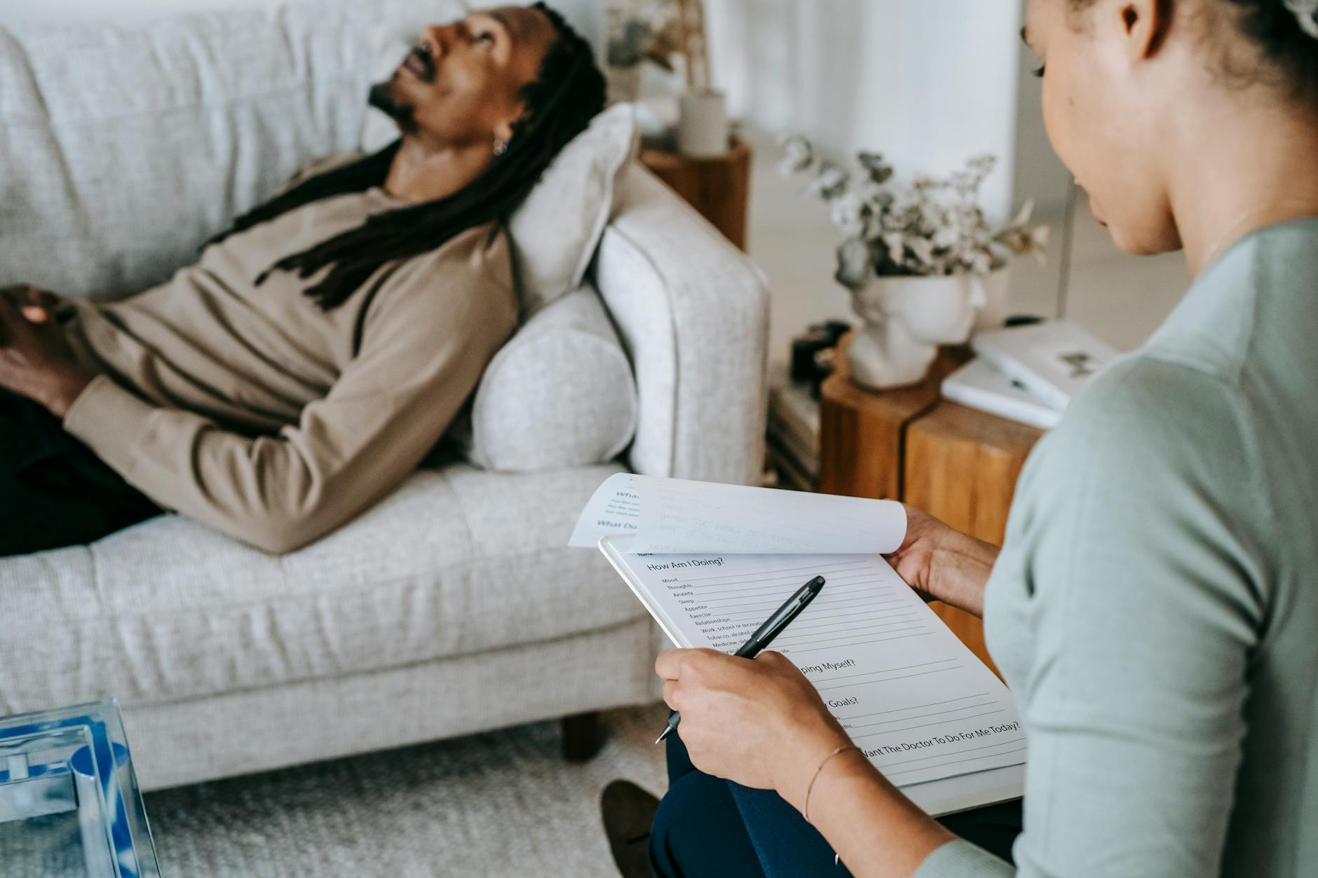 Crop anonymous African American female with paper form talking to male partner during psychotherapy in living room - mental well-being therapy
