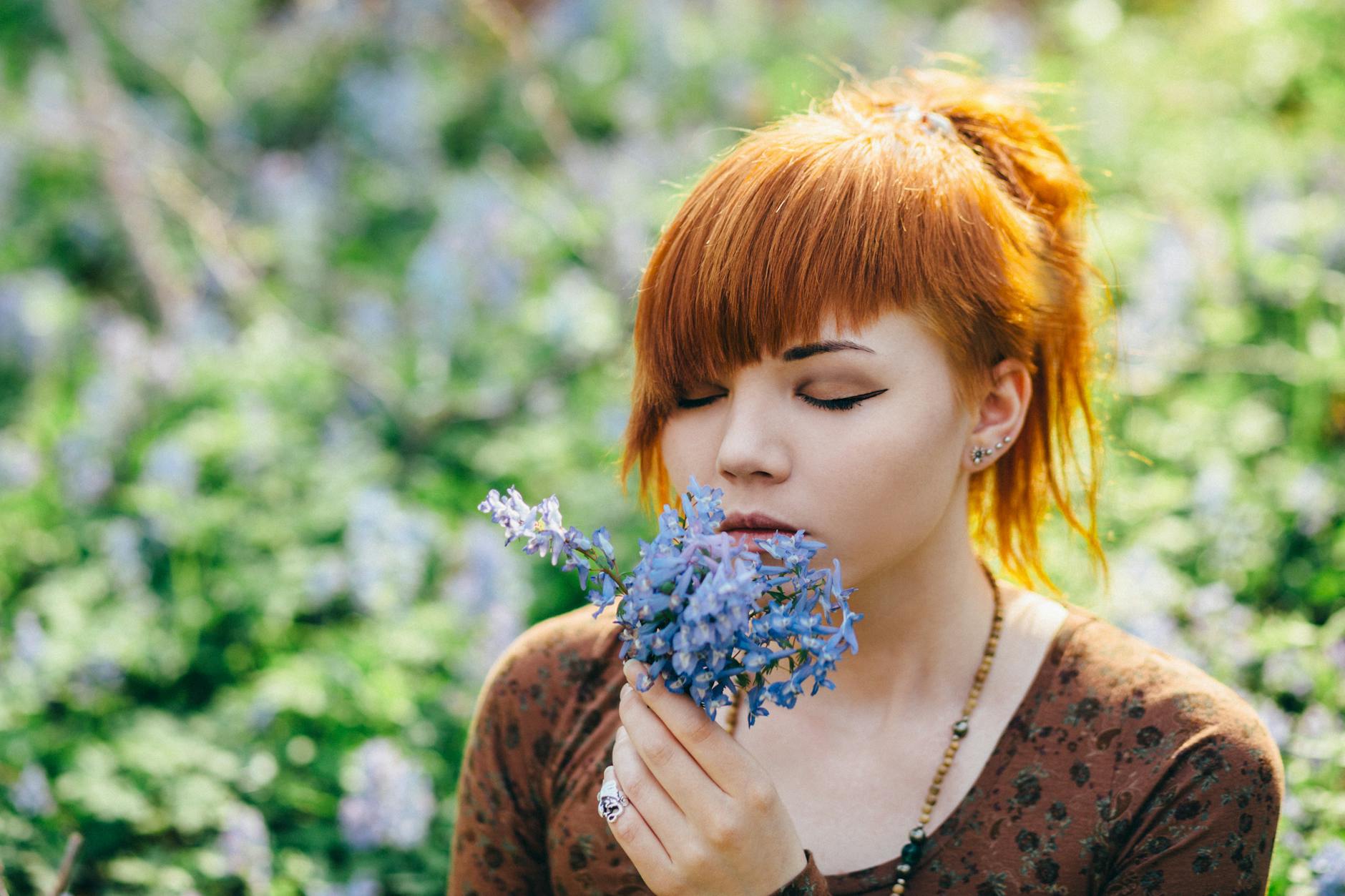Serene young woman with eyes closed holding and smelling delicate spring flowers. - mindfulness spring allergies