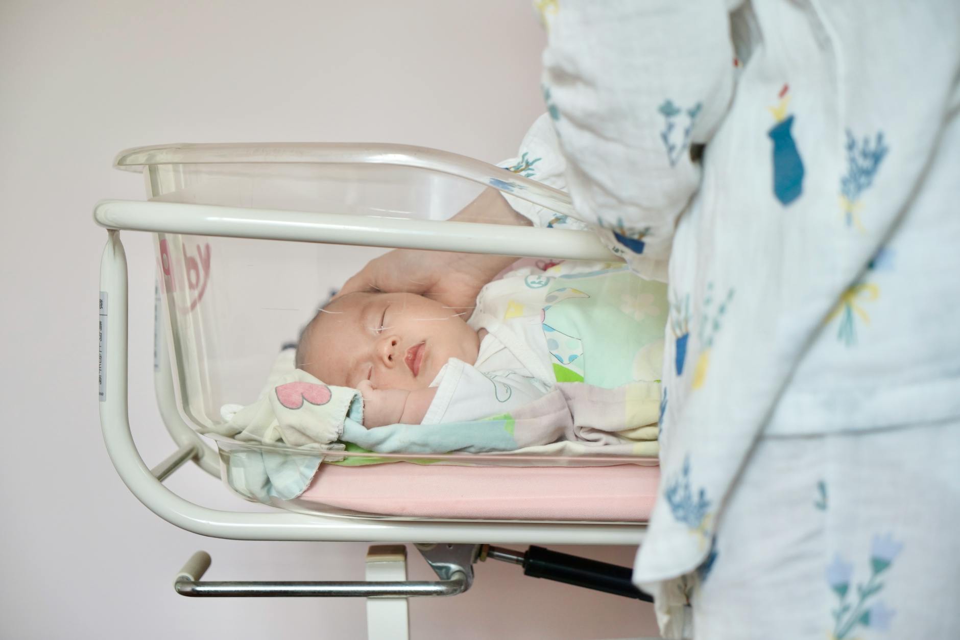 A tender moment of a newborn baby sleeping peacefully in a hospital bassinet being gently touched by a parent. - new parent exhaustion