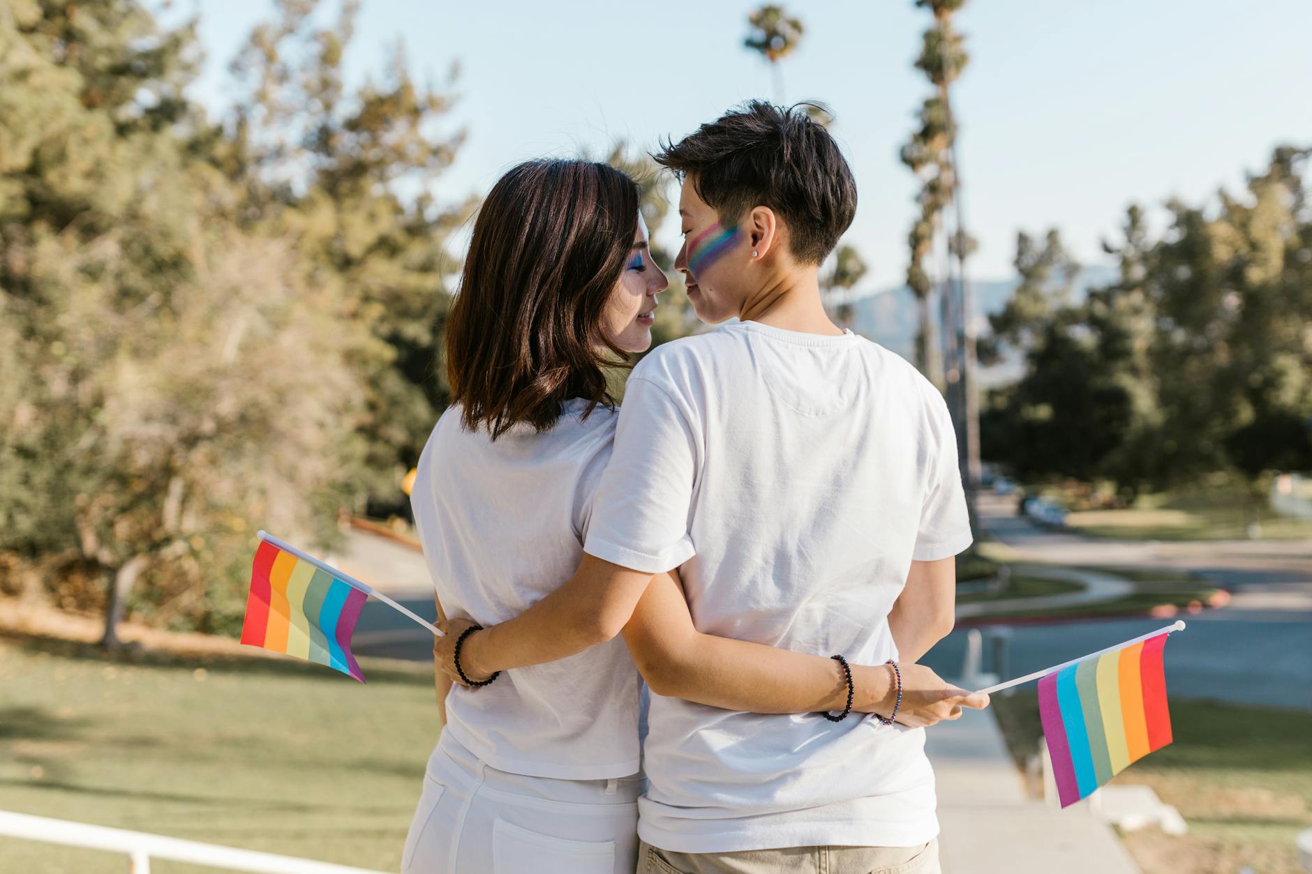 A loving couple embraces outdoors, holding rainbow flags, symbolizing LGBT pride and togetherness. - red flags relationships