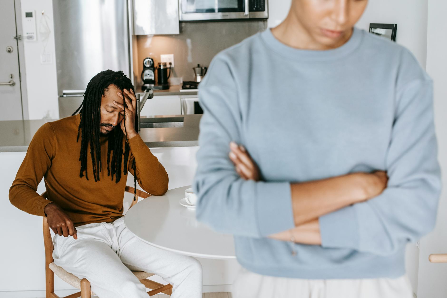 Young black guy sitting at table and having conflict with lady in light room - relationship resentment