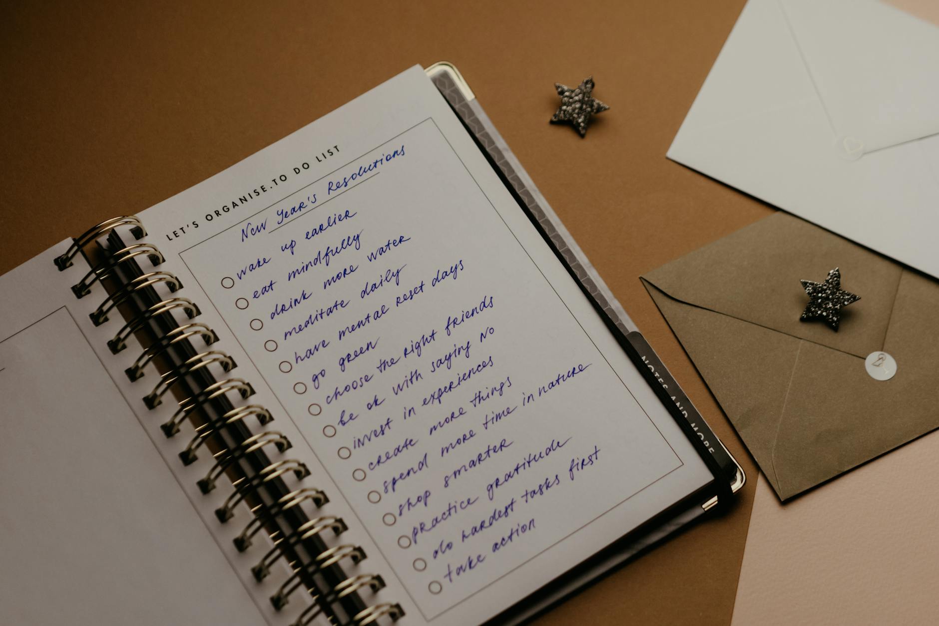 Spiral planner open to a page with handwritten New Year's resolutions and envelopes nearby. - what is a resolution
