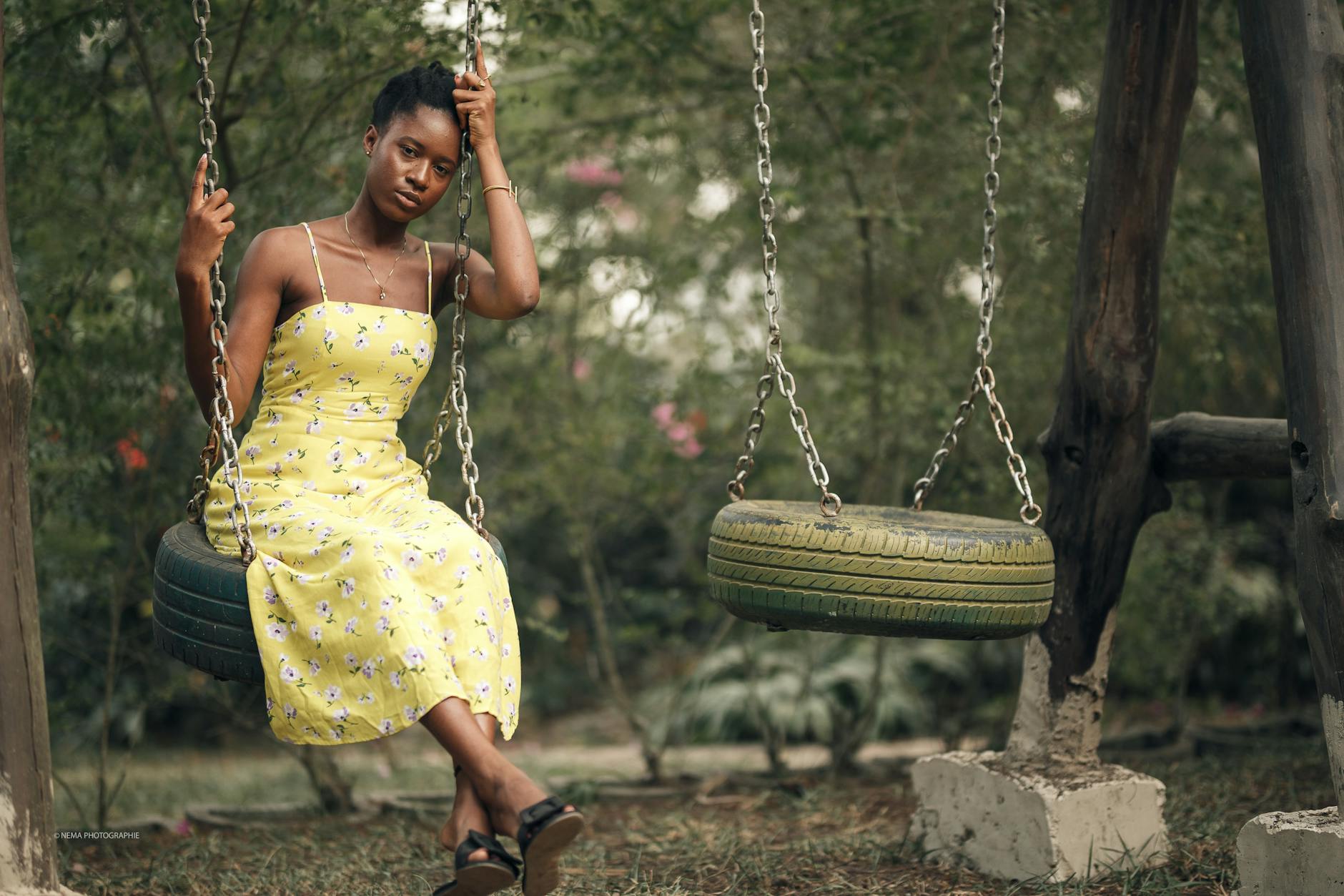 A woman in a yellow floral dress poses on a tire swing outdoors. - seasonal mood swings