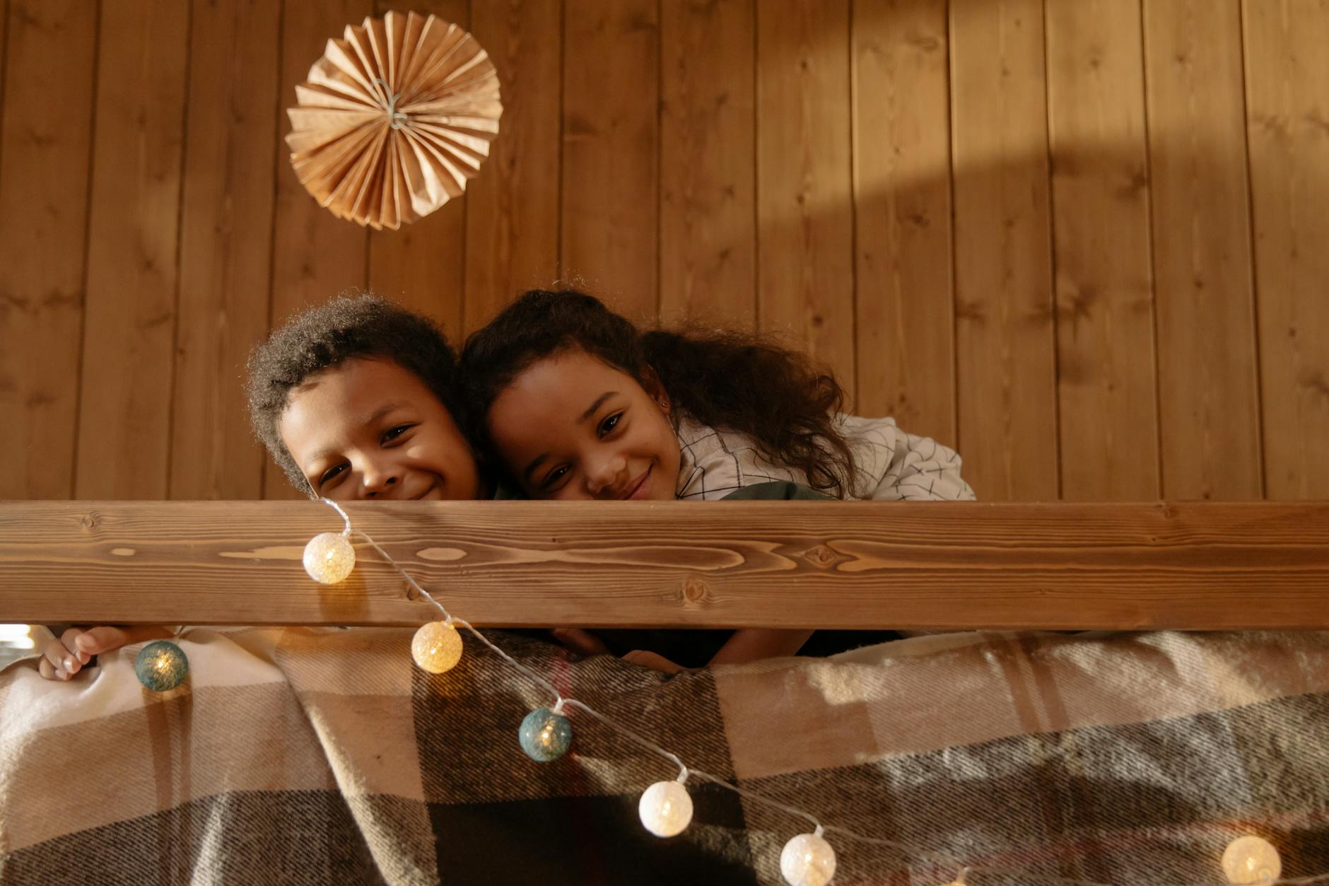Two happy children cuddling on a cozy indoor bed with warm lighting. - sibling rivalry causes