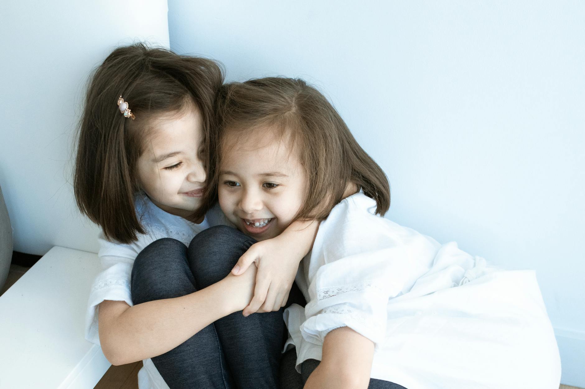 Two young girls in white tops embrace joyfully indoors, capturing sibling love and happiness. - sibling rivalry quotes