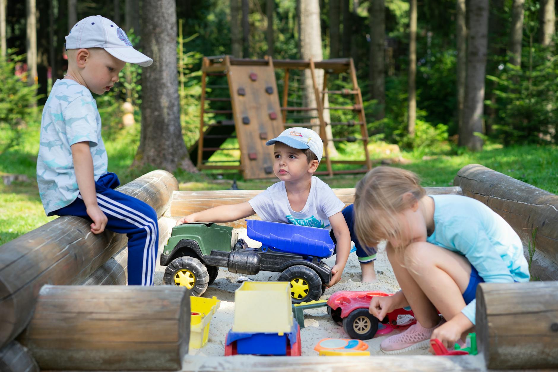 Three children engaged in imaginative play in an outdoor sandbox with toys. - social skills playdates