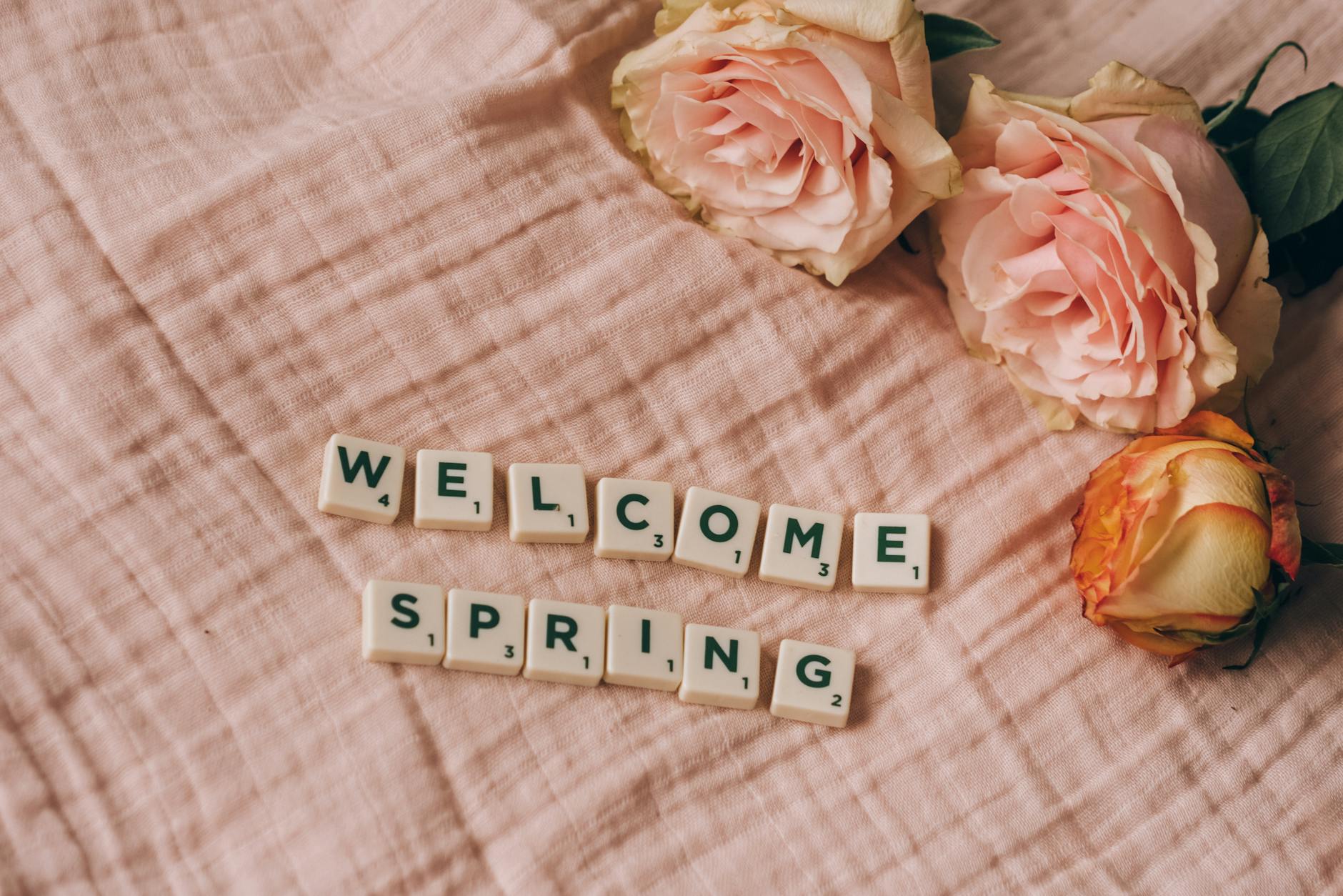 Pink roses and scrabble tiles spelling 'Welcome Spring' on a soft pink fabric background. - spring anxiety therapy