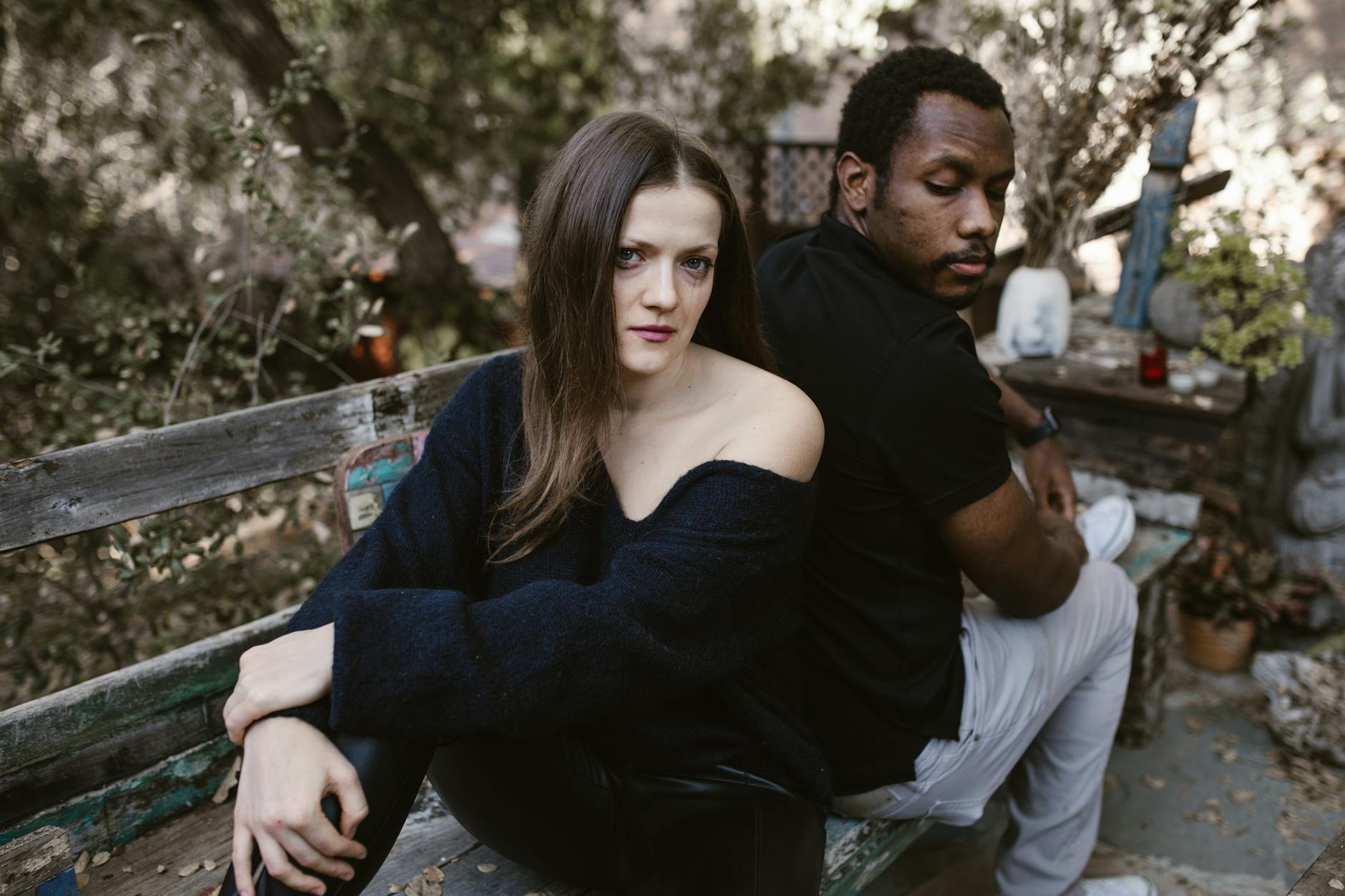 A couple sitting back to back on a rustic outdoor bench, showcasing emotions. - spring sad couples