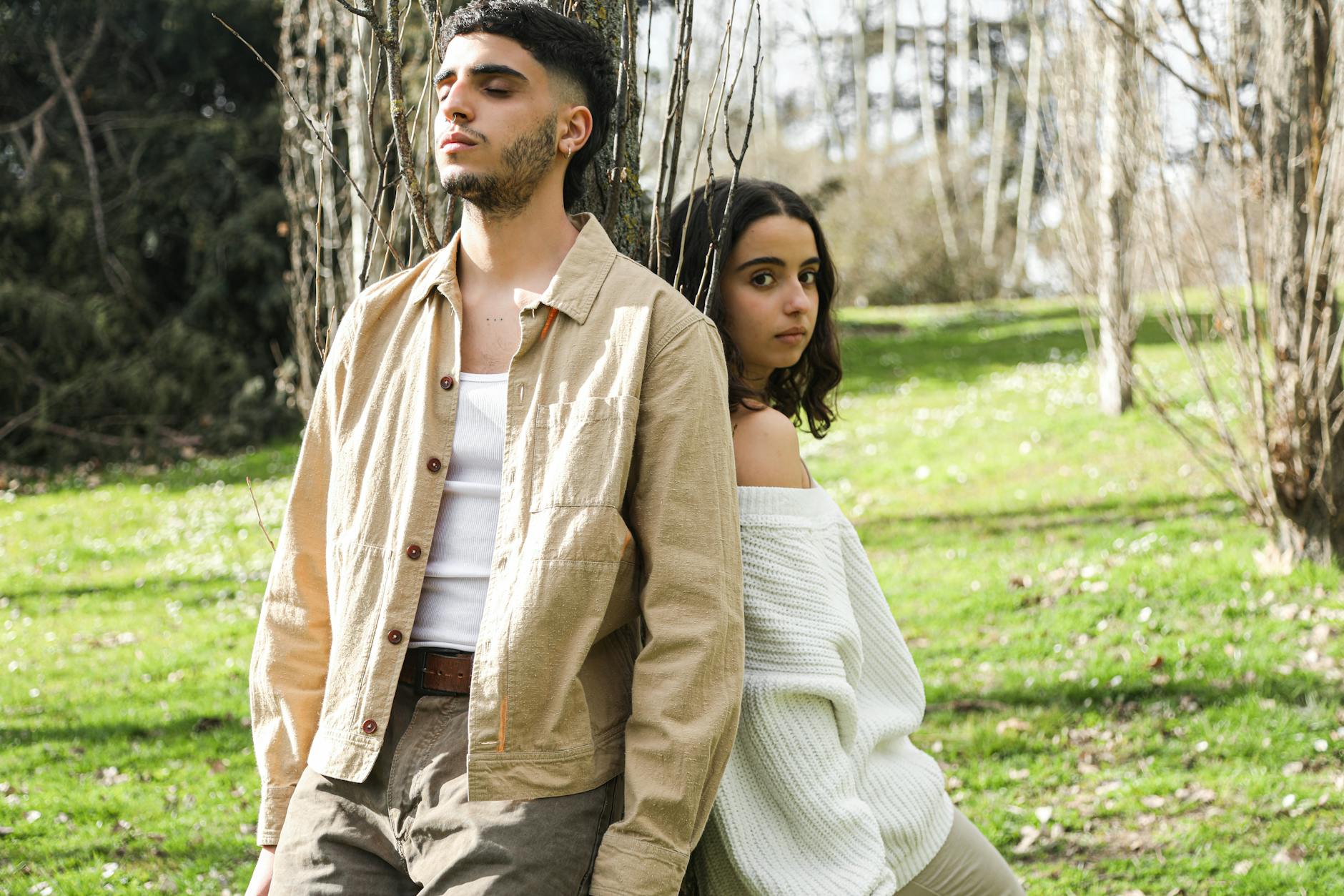 A young couple leaning against a tree in a sunlit park, enjoying a relaxing moment. - spring sad couples