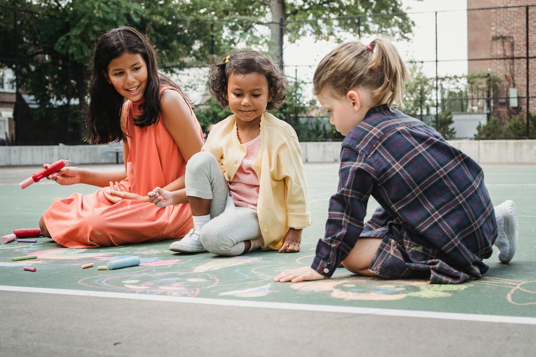 Three children drawing with chalk on a sunny outdoor court. Fun and creativity in action. - spring social skills
