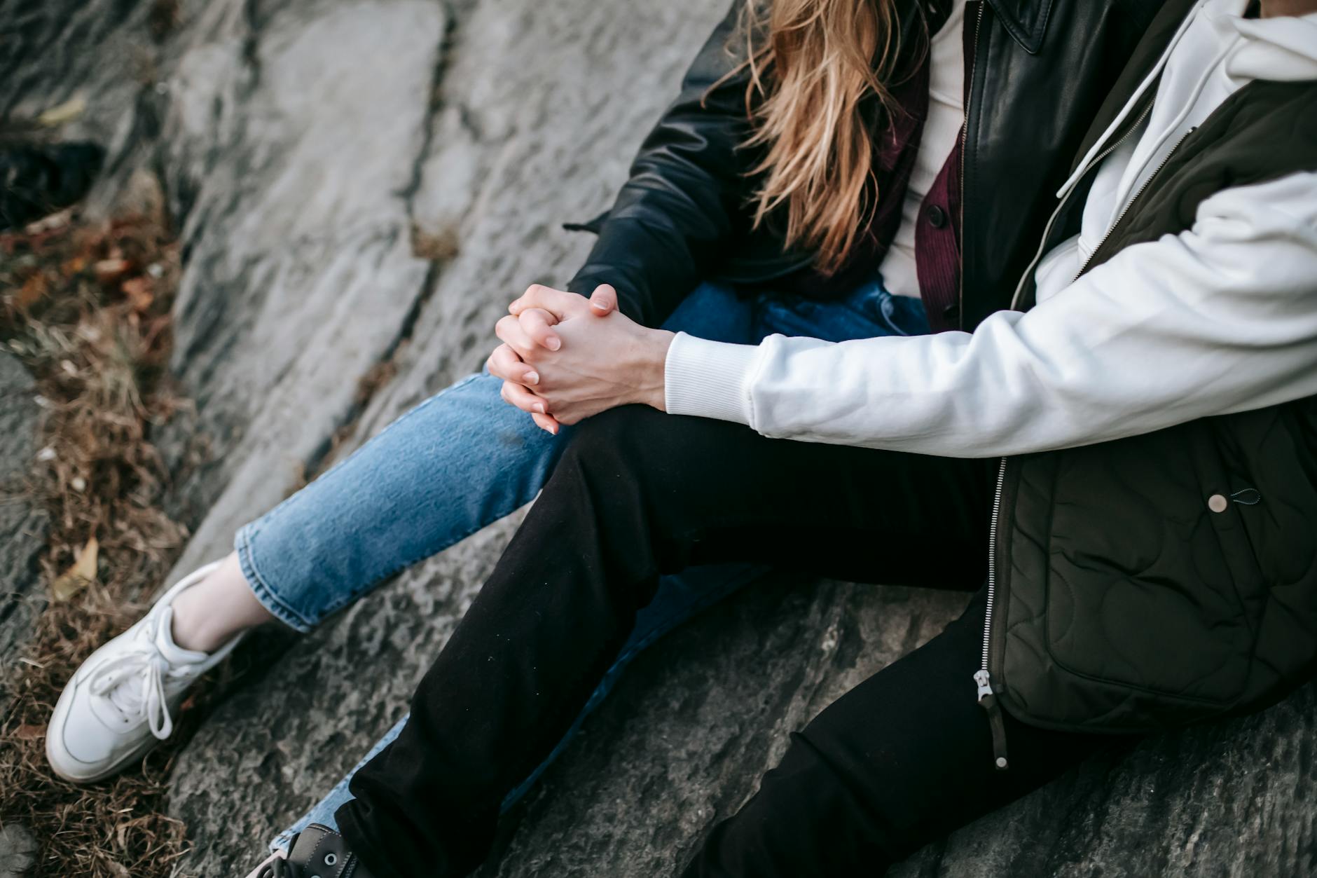 From above of crop unrecognizable couple in casual warm clothes sitting on rocky slope hugging and holding hands - vulnerability in relationships