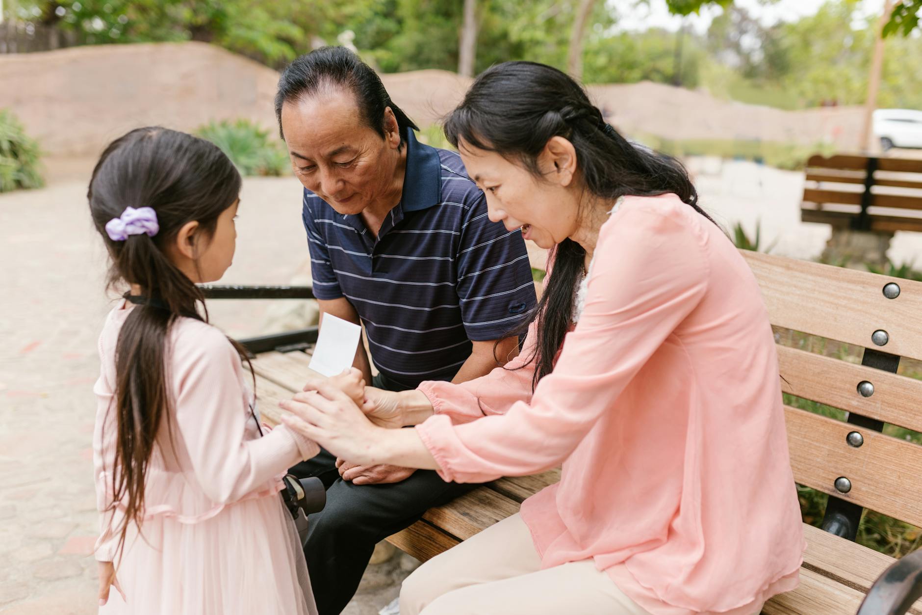 Asian family bonding outdoors, with adults sitting on a bench engaging with a child. - active listening family