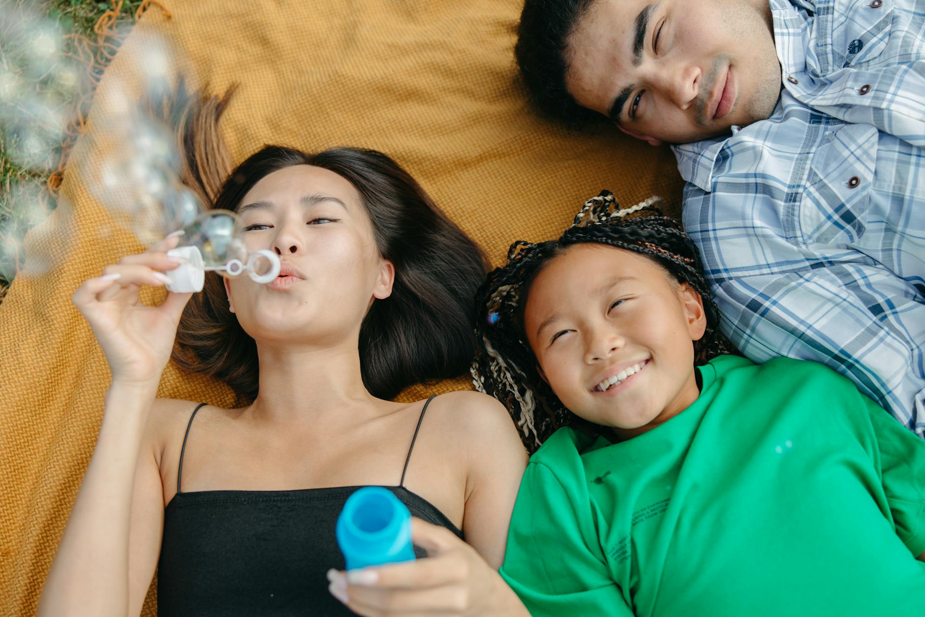 A joyful family scene with parents and daughter enjoying the outdoors and blowing bubbles. - co-parenting after break