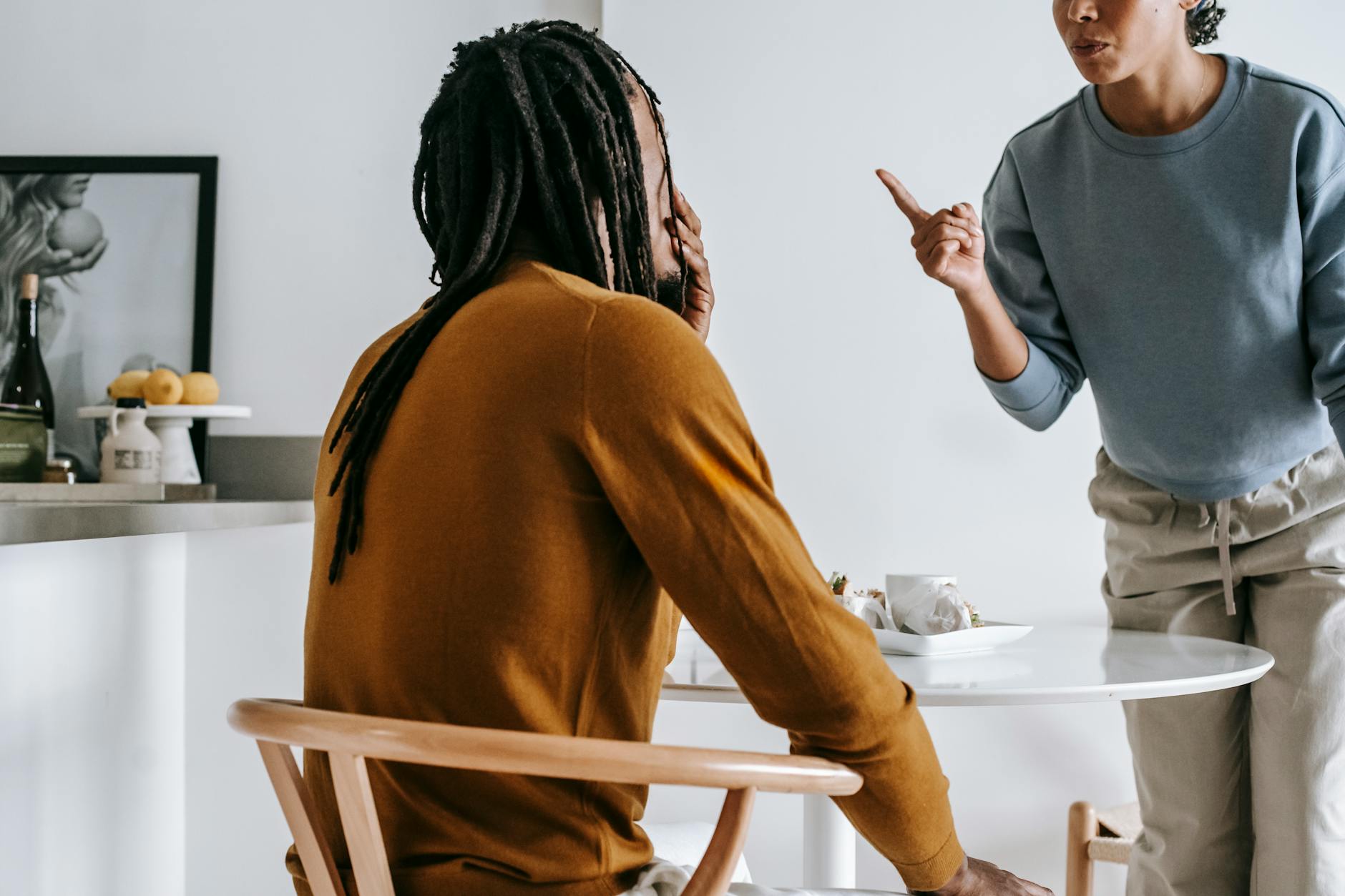 Young African American lady standing near table while having argument with guy sitting at kitchen - conflict resolution worksheet