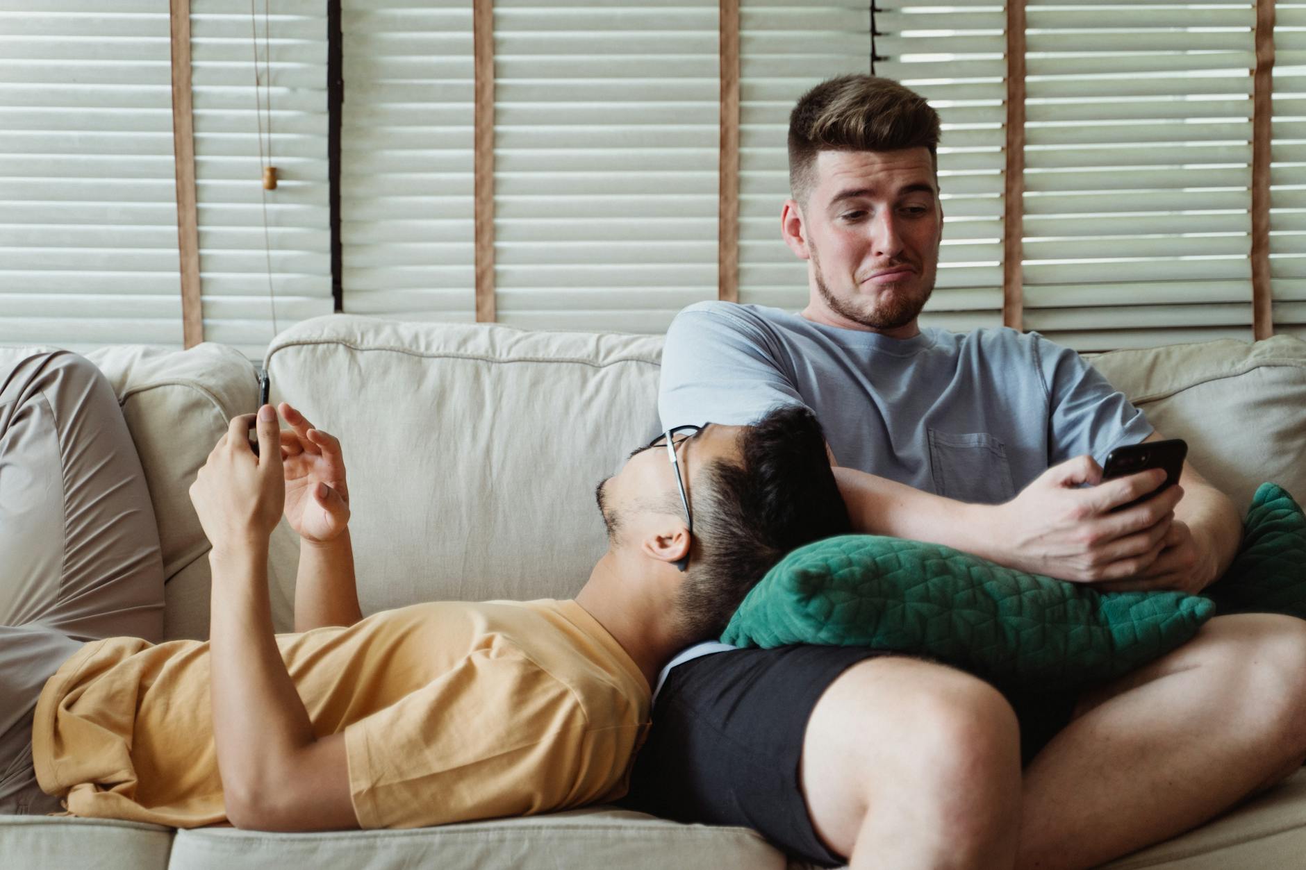 Interracial gay couple enjoying leisure time on a sofa with smartphones, indoors. - couples therapy boredom