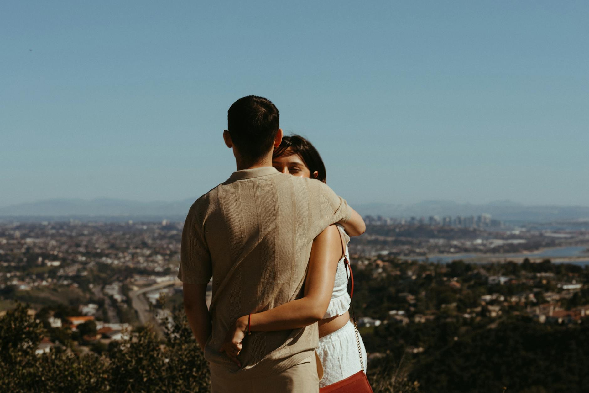 Young couple embracing with a scenic view of a city skyline in the background, captured on a sunny day. - couples therapy goals