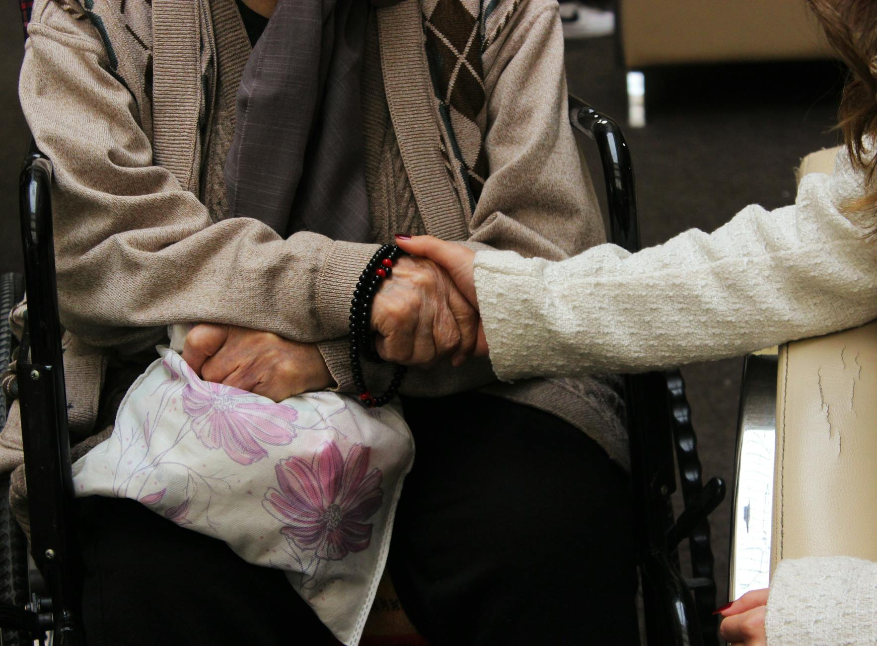 Elderly woman in wheelchair warmly holding another's hand, symbolizing care and support. - family communication empathy