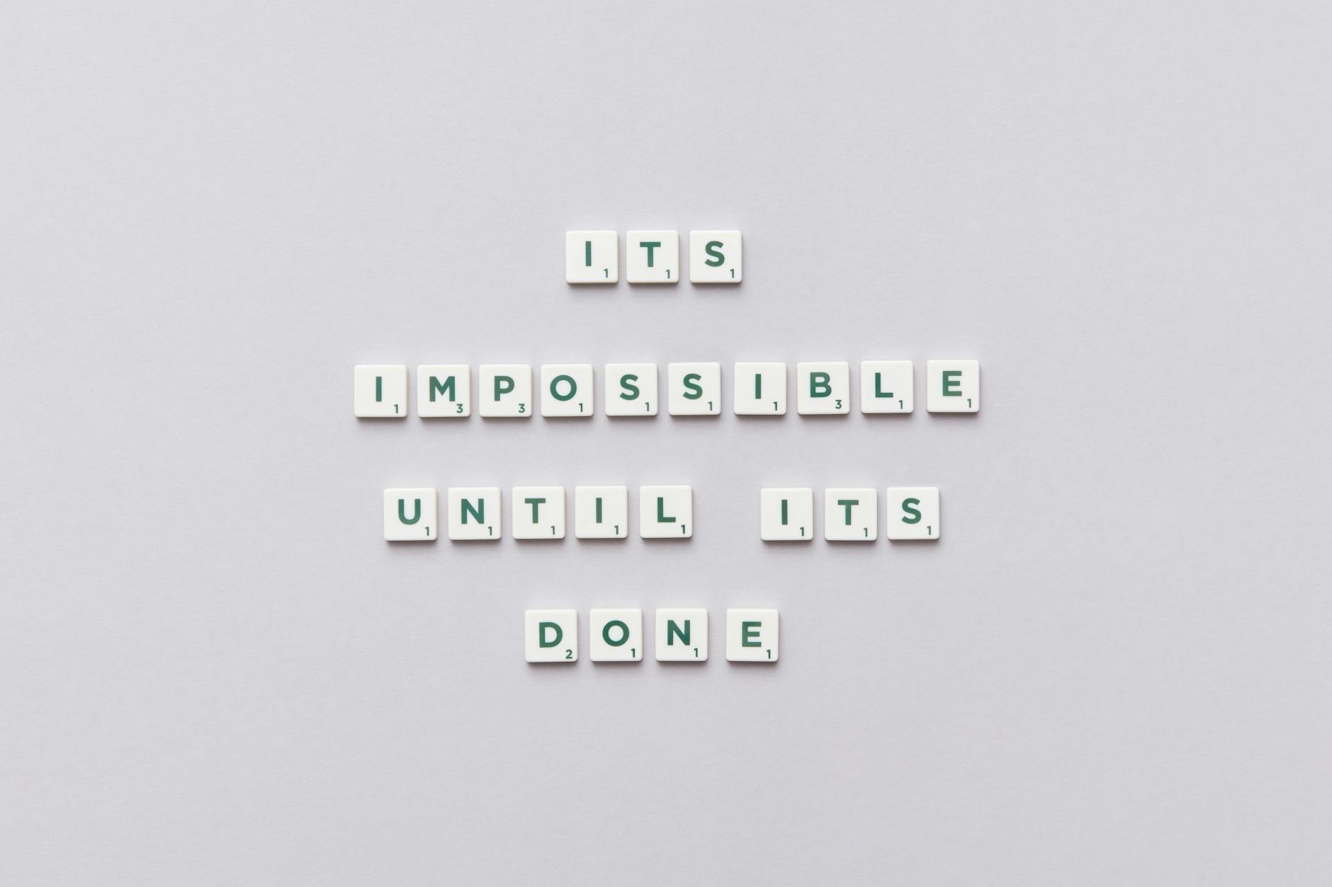 Motivational phrase 'It's impossible until it's done' arranged with Scrabble tiles on a gray background. - overcome perfectionism