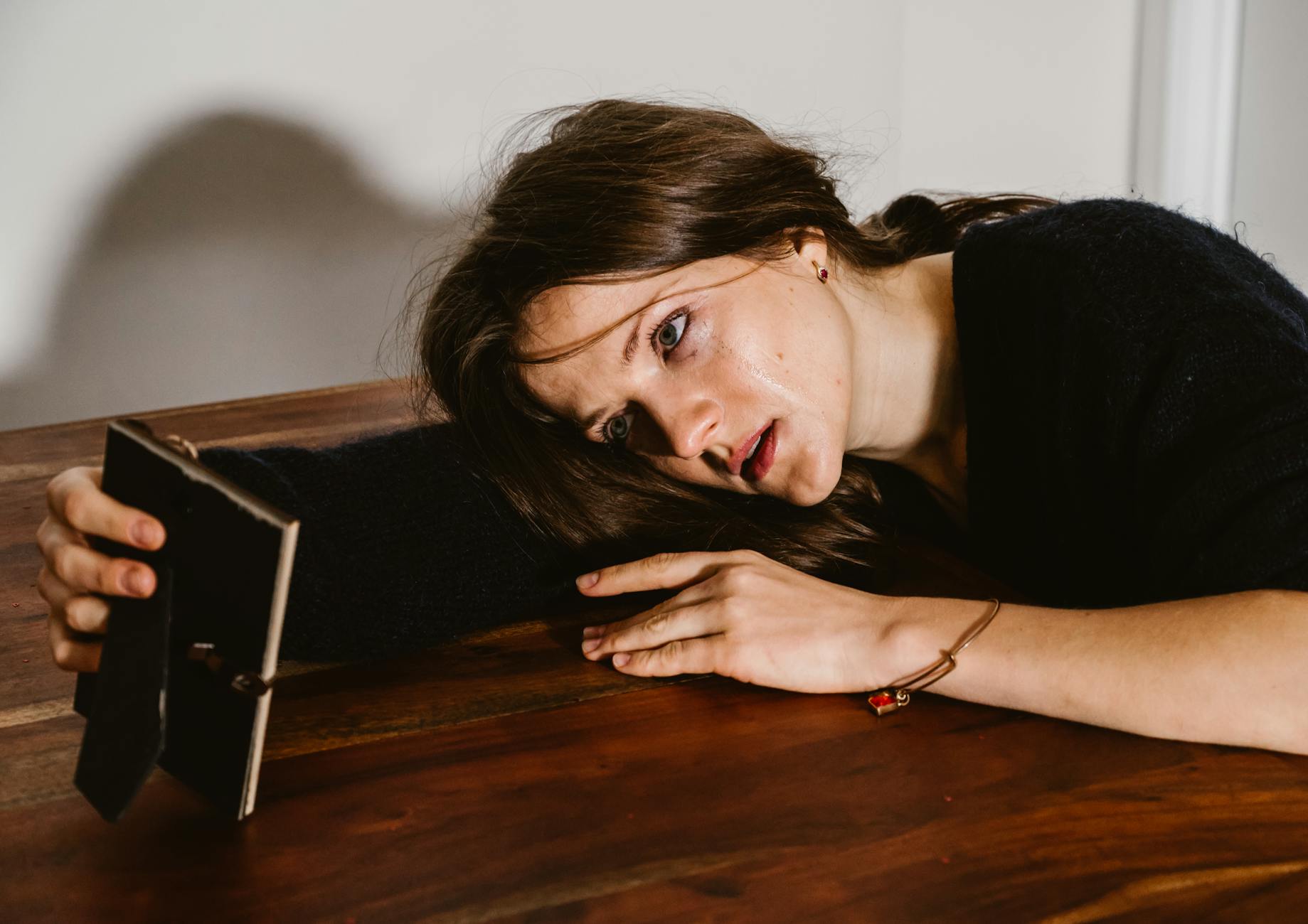A woman in emotional distress lays on a wooden table holding a picture frame. - post breakup healing