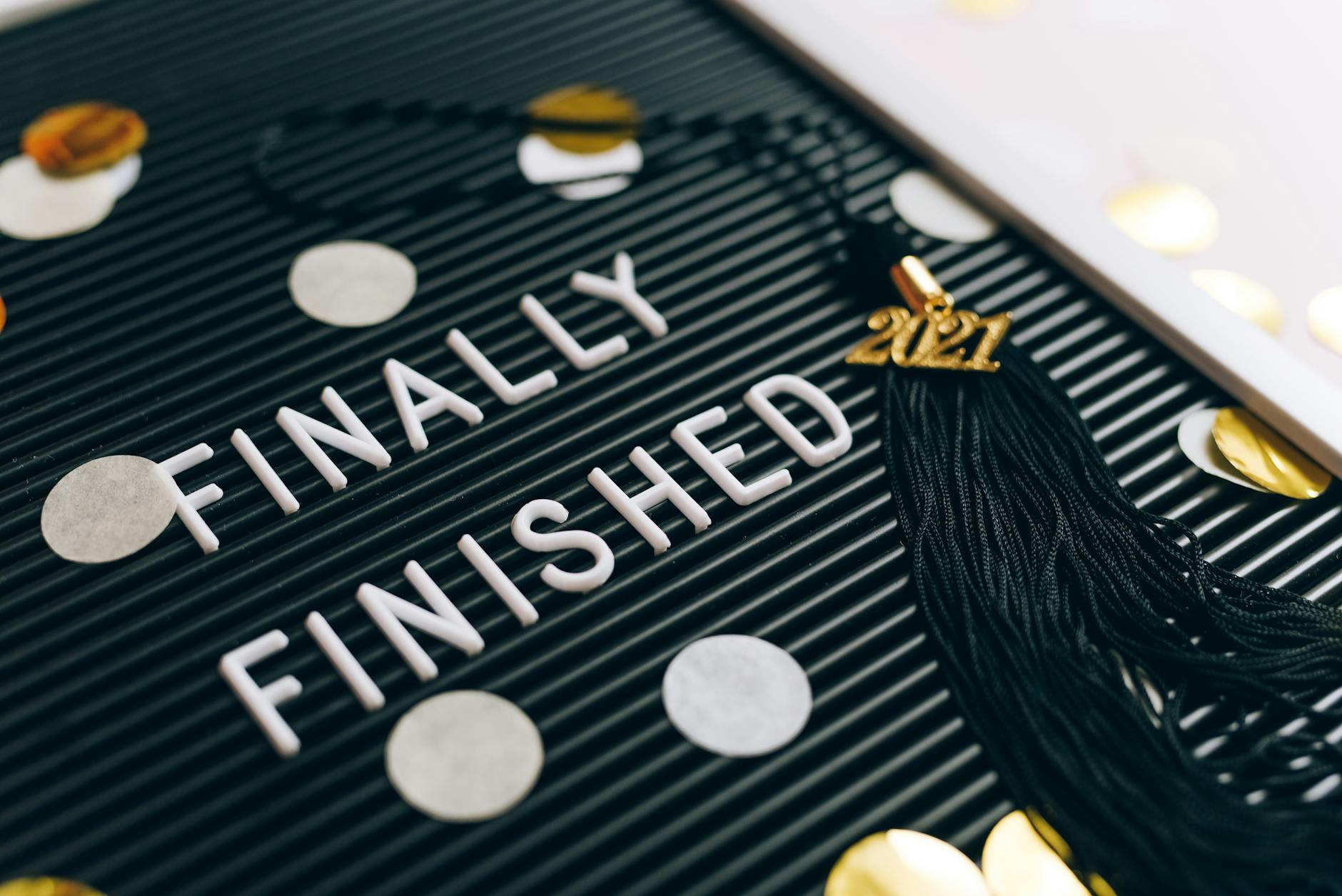 Close-up of 'Finally Finished' sign with graduation tassel and 2021 charm on letter board. - post grad adjustment