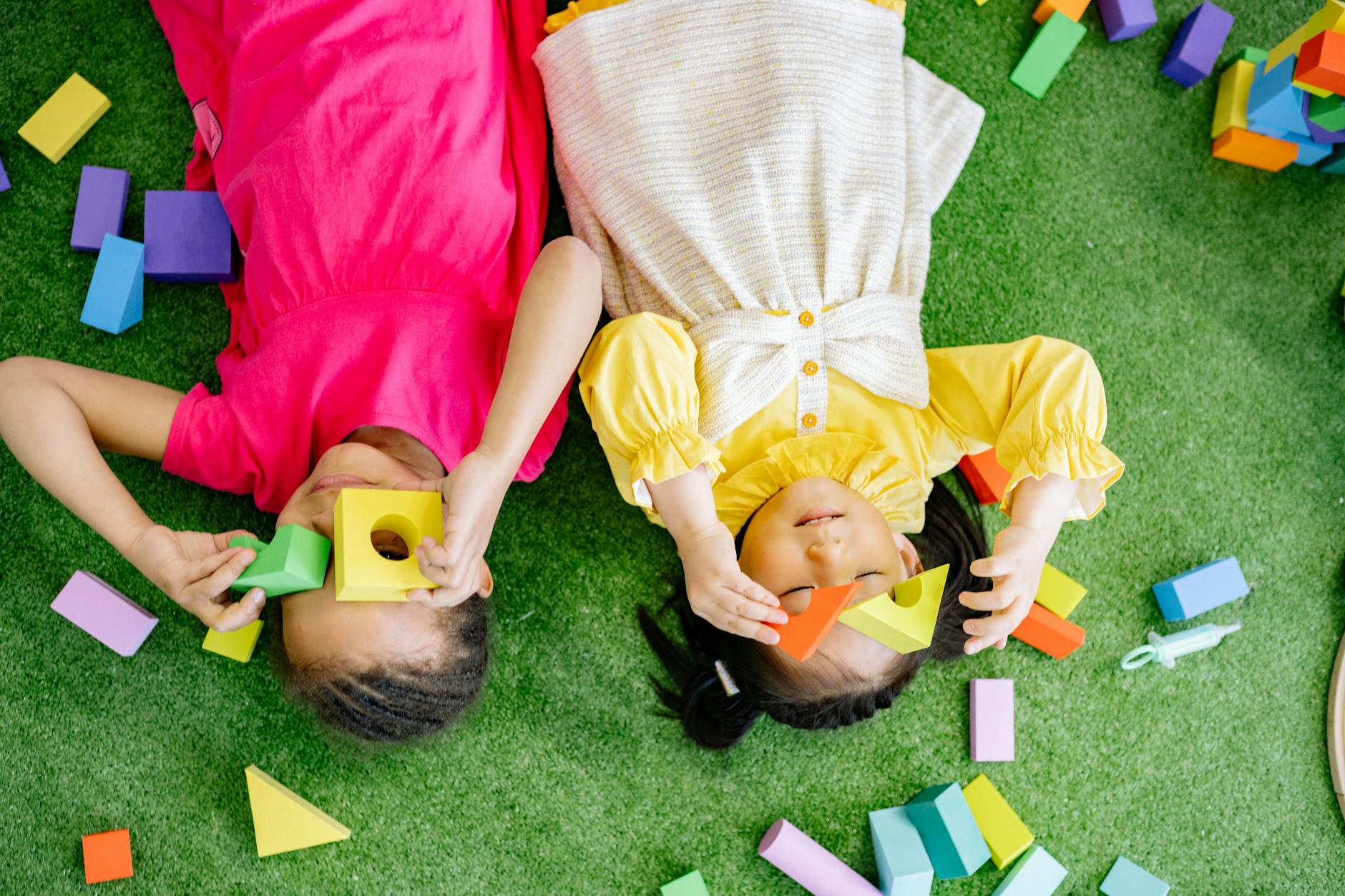 Two joyful kids playing with colorful wooden blocks on a green surface indoors. - preschool garden activities