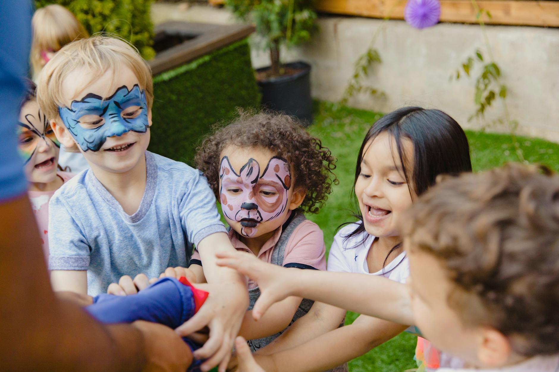 Group of children with face paint enjoying playtime outdoors, laughing and engaging in games. - preschool playdate ideas